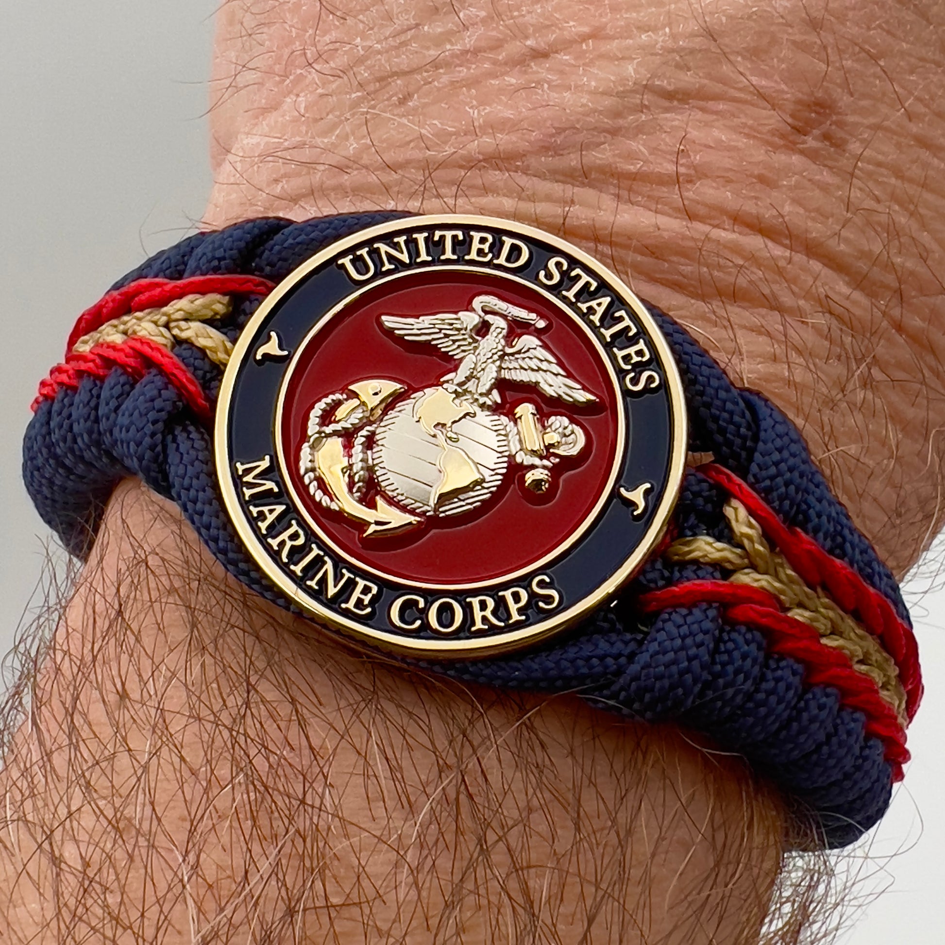 Thick and comfortable braided United States Marine Corps bracelet featuring a 24K gold and silver plated USMC officer Eagle Globe and Anchor medallion, a Cobra style tactical buckle and woven with Navy blue, Imperial red and gold paracord.
