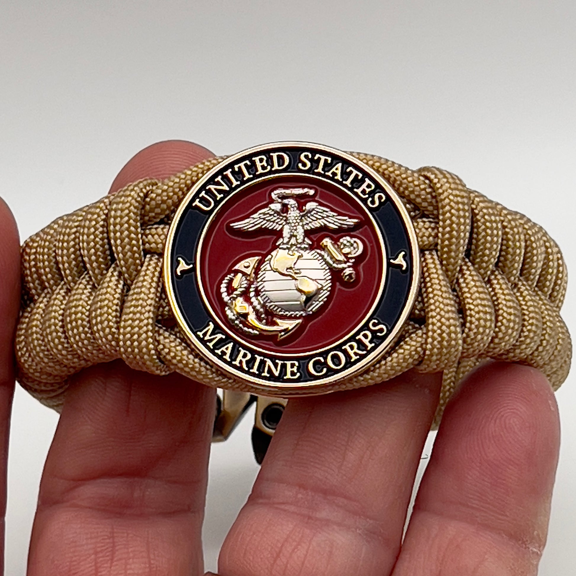 Thick and comfortable braided United States Marine Corps bracelet featuring a 24K gold and silver plated USMC officer Eagle Globe and Anchor medallion, a Cobra style tactical buckle and woven with gold 550 paracord.