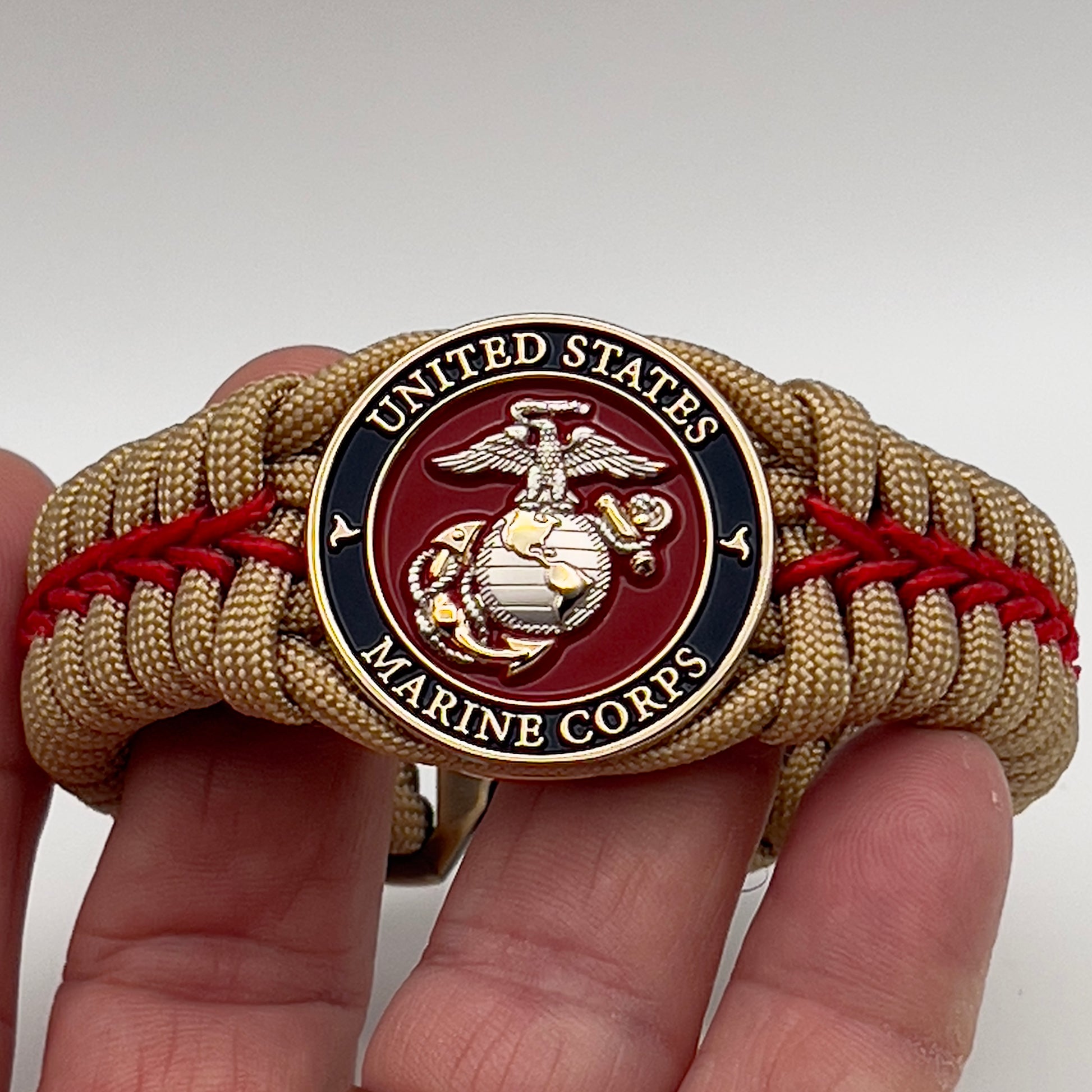 Thick and comfortable braided United States Marine Corps bracelet featuring a 24K gold and silver plated USMC officer Eagle Globe and Anchor medallion, a Cobra style tactical buckle and woven with gold 550 and Imperial red micro paracord.