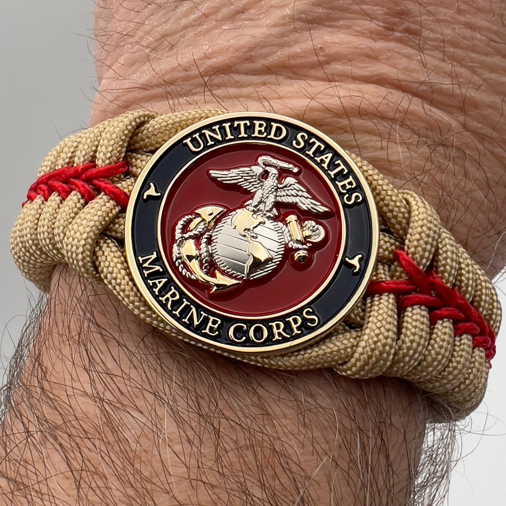 Thick and comfortable braided United States Marine Corps bracelet featuring a 24K gold and silver plated USMC officer Eagle Globe and Anchor medallion, a Cobra style tactical buckle and woven with gold 550 and Imperial red micro paracord.