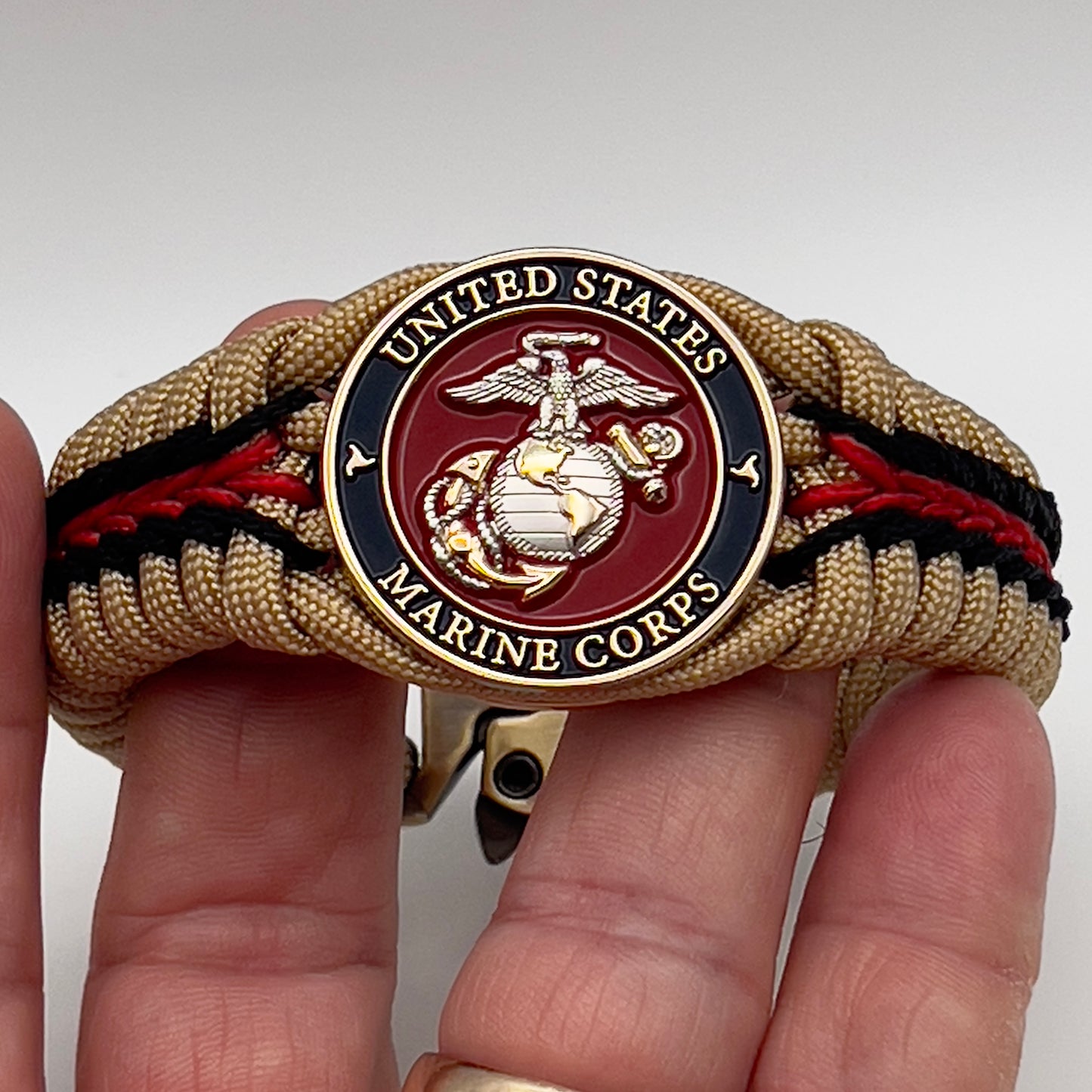 Thick and comfortable braided United States Marine Corps bracelet featuring a 24K gold and silver plated USMC officer Eagle Globe and Anchor medallion, a Cobra style tactical buckle and woven with gold 550 and Imperial red micro paracord.