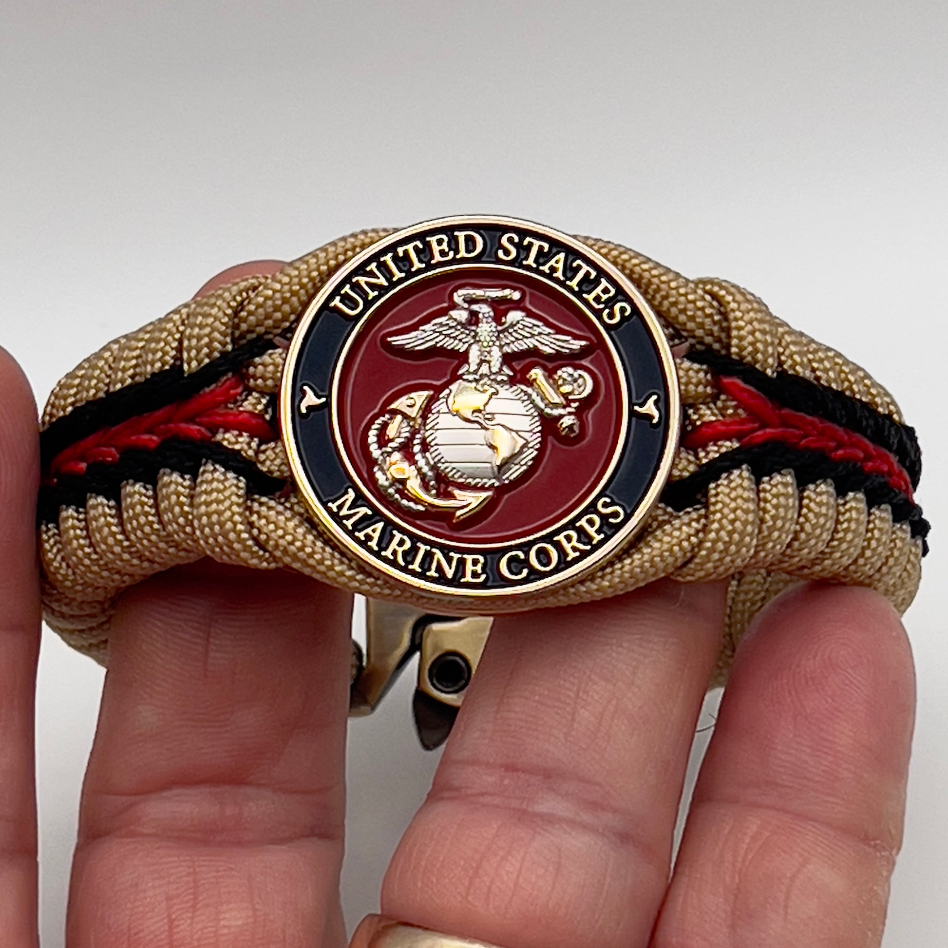 Thick and comfortable braided United States Marine Corps bracelet featuring a 24K gold and silver plated USMC officer Eagle Globe and Anchor medallion, a Cobra style tactical buckle and woven with gold 550 and Imperial red micro paracord.