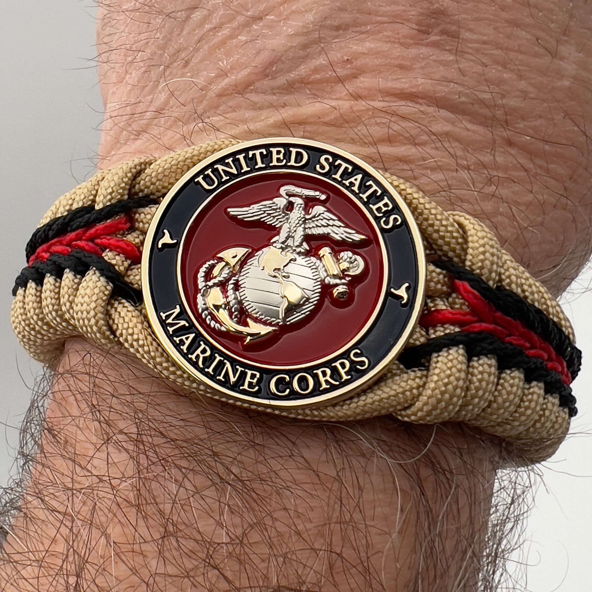 Thick and comfortable braided United States Marine Corps bracelet featuring a 24K gold and silver plated USMC officer Eagle Globe and Anchor medallion, a Cobra style tactical buckle and woven with gold 550 and Imperial red micro paracord.