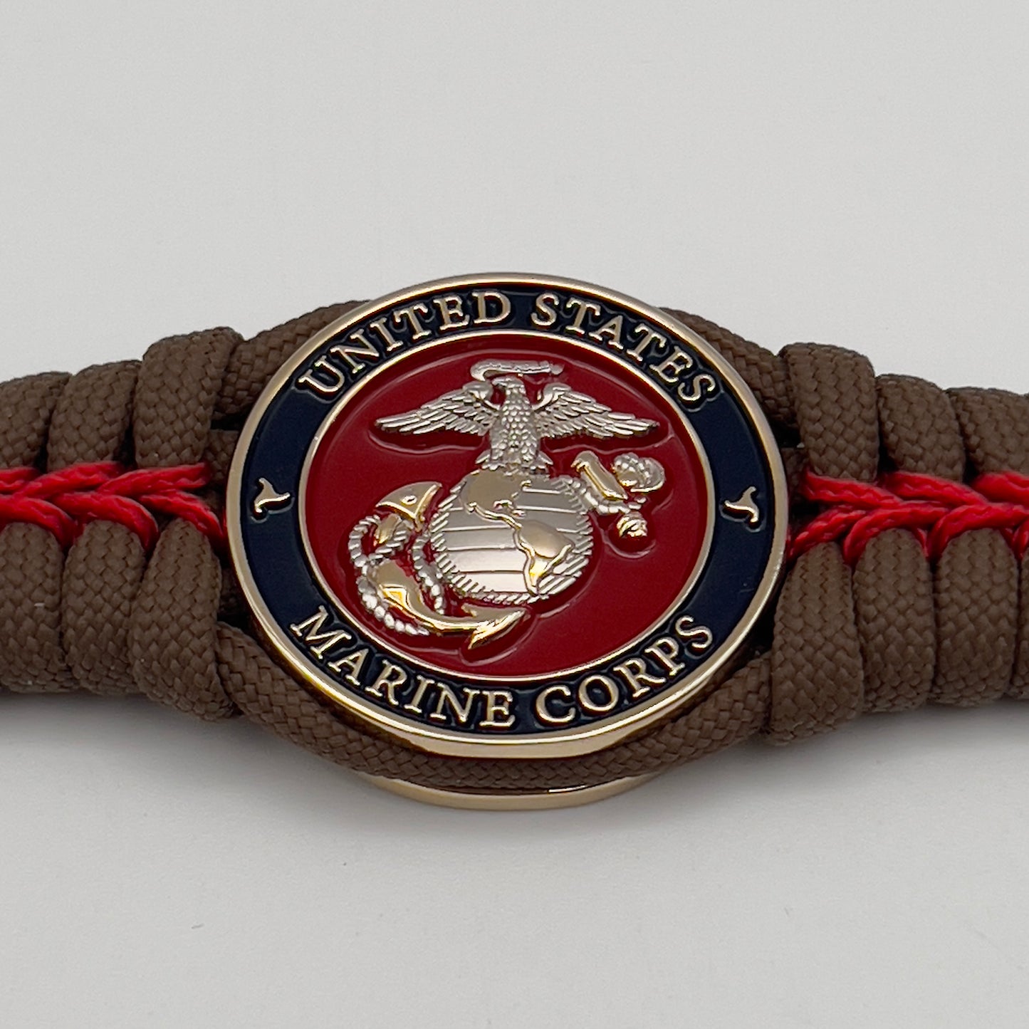 Thick, semi-rigid and comfortable braided United States Marine Corps bracelet featuring a 24K gold and silver plated USMC officer Eagle Globe and Anchor medallion, a Cobra style tactical buckle and woven with Coyote brown 550 and Imperial red micro paracord.