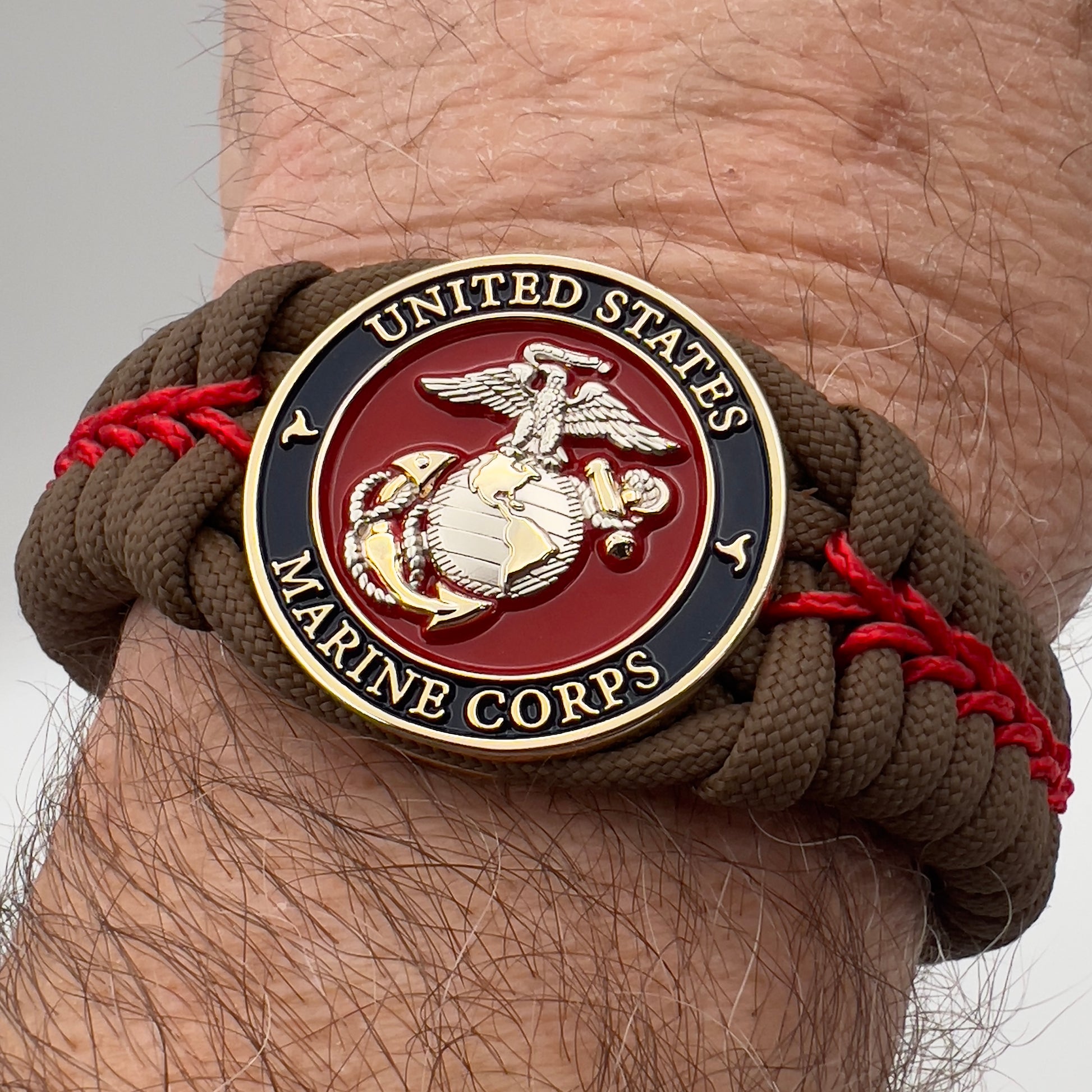 Thick, semi-rigid and comfortable braided United States Marine Corps bracelet featuring a 24K gold and silver plated USMC officer Eagle Globe and Anchor medallion, a Cobra style tactical buckle and woven with Coyote brown 550 and Imperial red micro paracord.