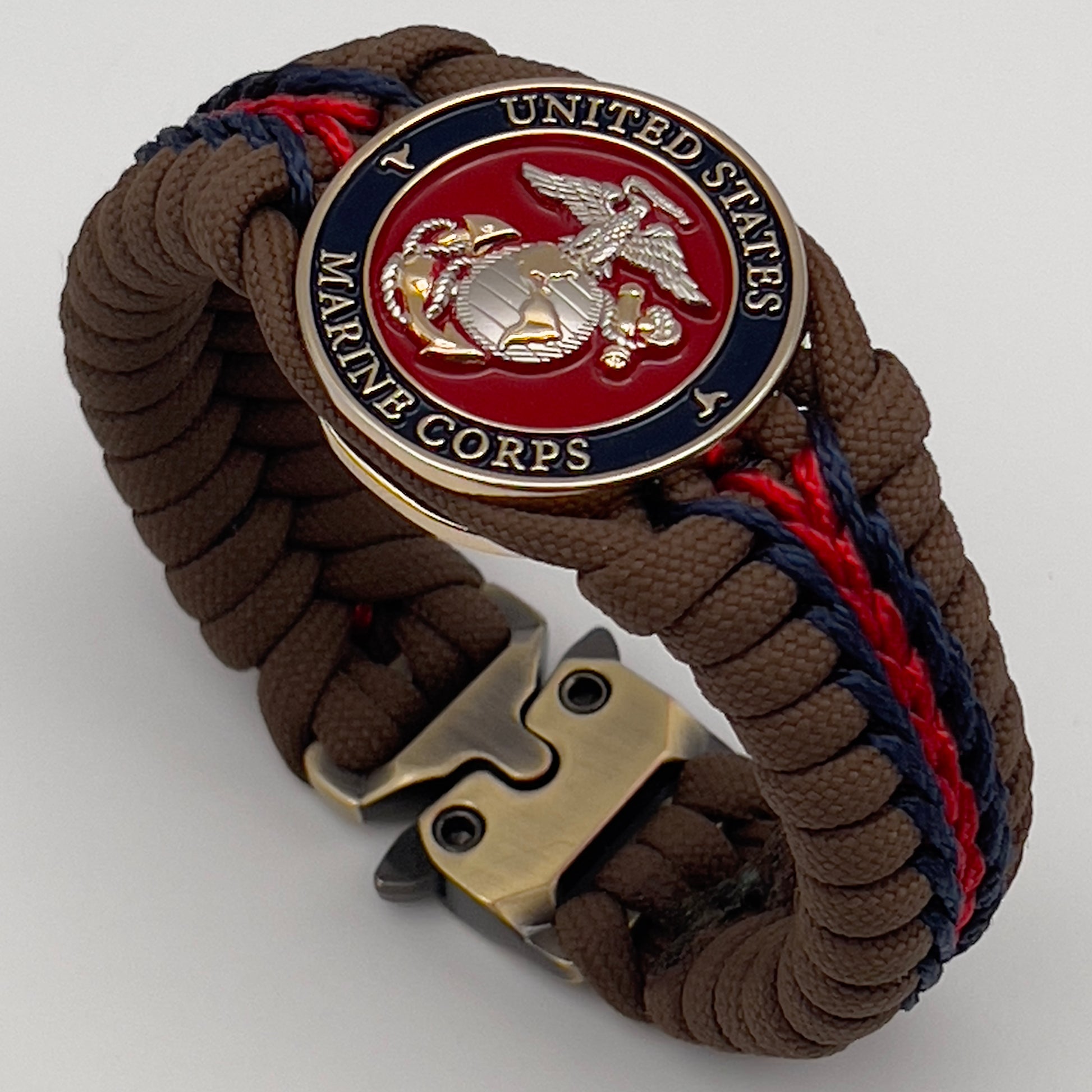 Thick, semi-rigid and comfortable braided United States Marine Corps bracelet featuring a 24K gold and silver plated USMC officer Eagle Globe and Anchor medallion, a Cobra style tactical buckle and woven with Coyote brown 550, Navy blue and Imperial red micro paracord.