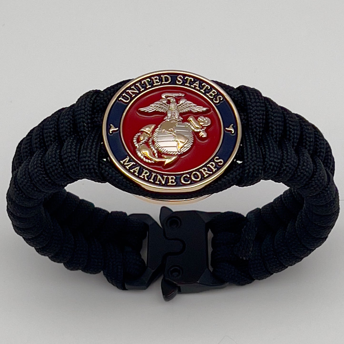 Thick, semi-rigid and comfortable braided United States Marine Corps bracelet featuring a 24K gold and silver plated USMC officer Eagle Globe and Anchor medallion, a black Cobra style tactical buckle and woven with black 550 paracord.