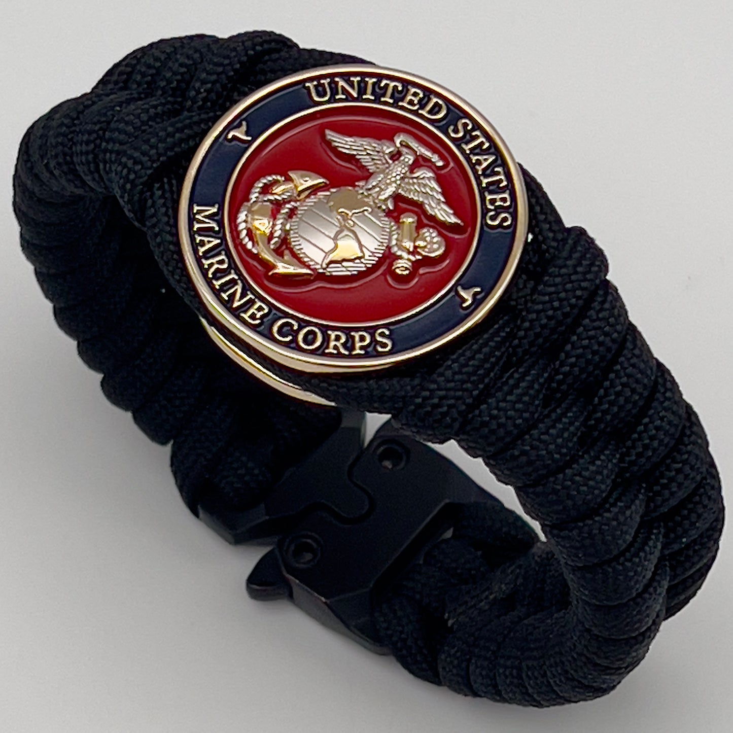 Thick, semi-rigid and comfortable braided United States Marine Corps bracelet featuring a 24K gold and silver plated USMC officer Eagle Globe and Anchor medallion, a black Cobra style tactical buckle and woven with black 550 paracord.
