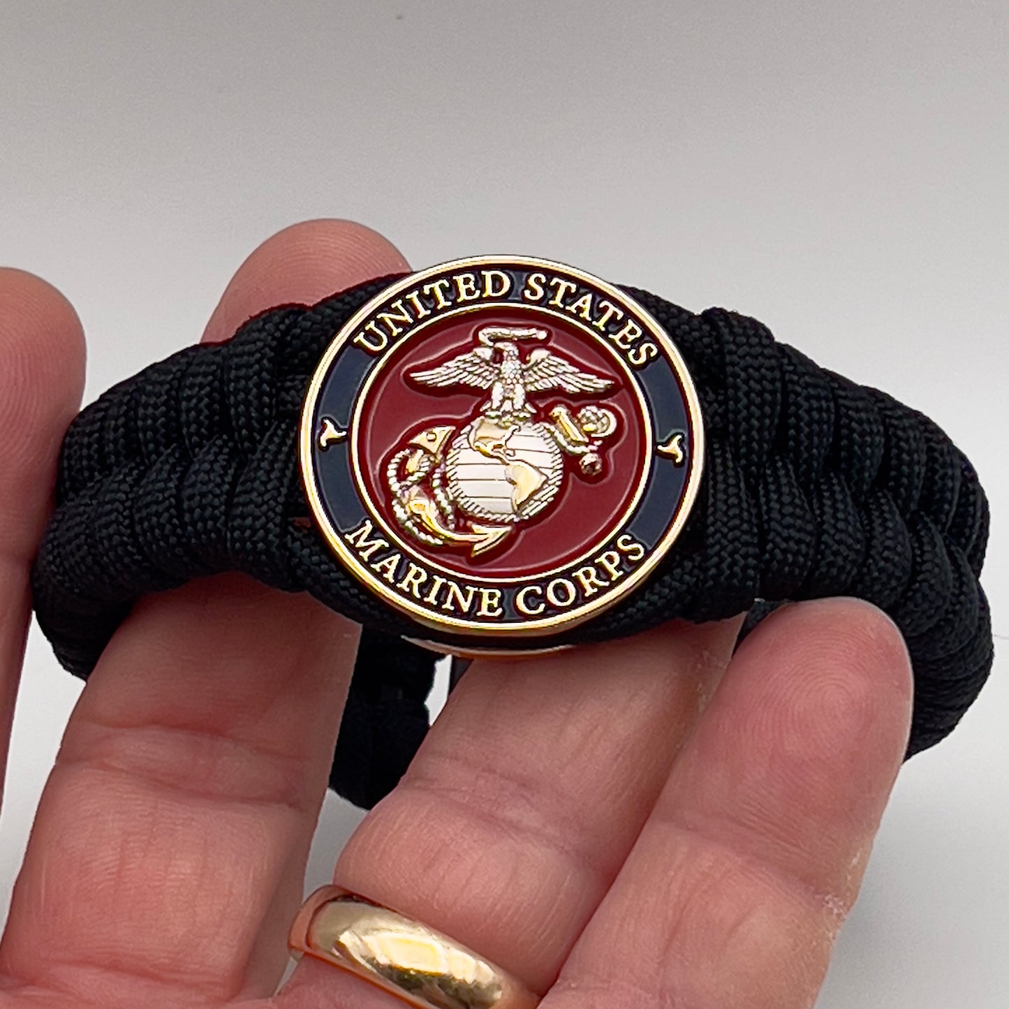 Thick, semi-rigid and comfortable braided United States Marine Corps bracelet featuring a 24K gold and silver plated USMC officer Eagle Globe and Anchor medallion, a black Cobra style tactical buckle and woven with black 550 paracord.