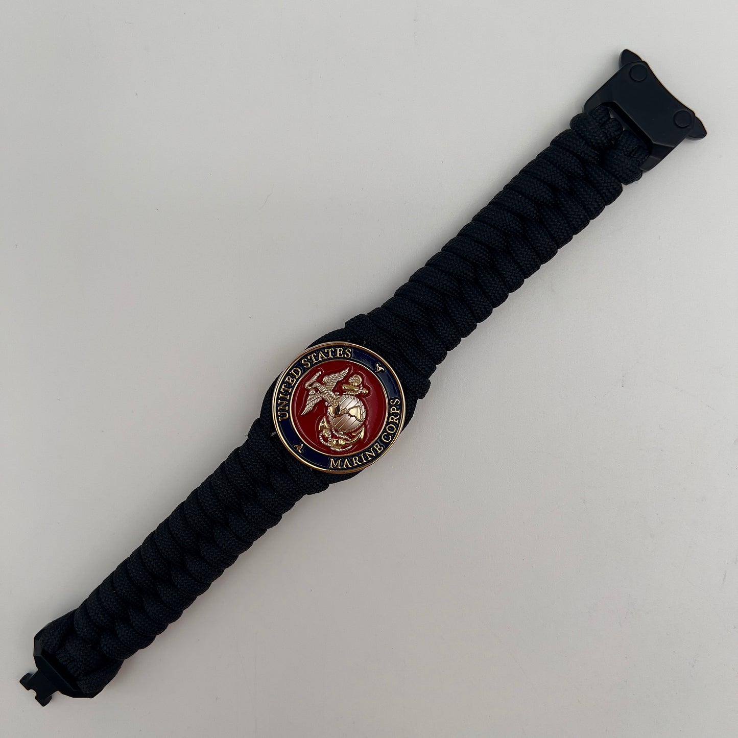 Thick, semi-rigid and comfortable braided United States Marine Corps bracelet featuring a 24K gold and silver plated USMC officer Eagle Globe and Anchor medallion, a black Cobra style tactical buckle and woven with black 550 paracord.