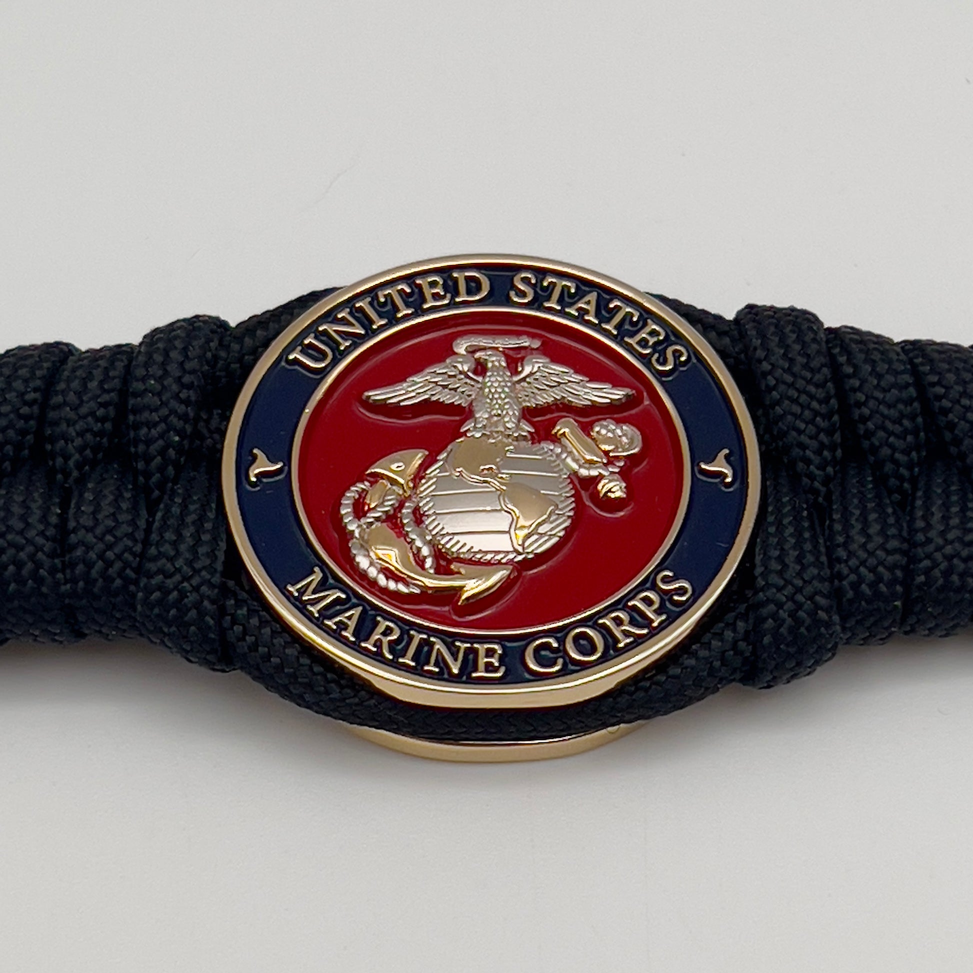 Thick, semi-rigid and comfortable braided United States Marine Corps bracelet featuring a 24K gold and silver plated USMC officer Eagle Globe and Anchor medallion, a black Cobra style tactical buckle and woven with black 550 paracord.