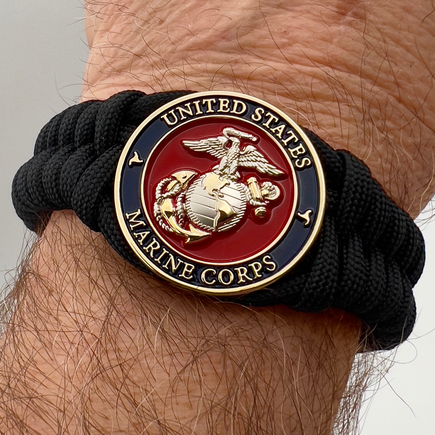 Thick, semi-rigid and comfortable braided United States Marine Corps bracelet featuring a 24K gold and silver plated USMC officer Eagle Globe and Anchor medallion, a black Cobra style tactical buckle and woven with black 550 paracord.