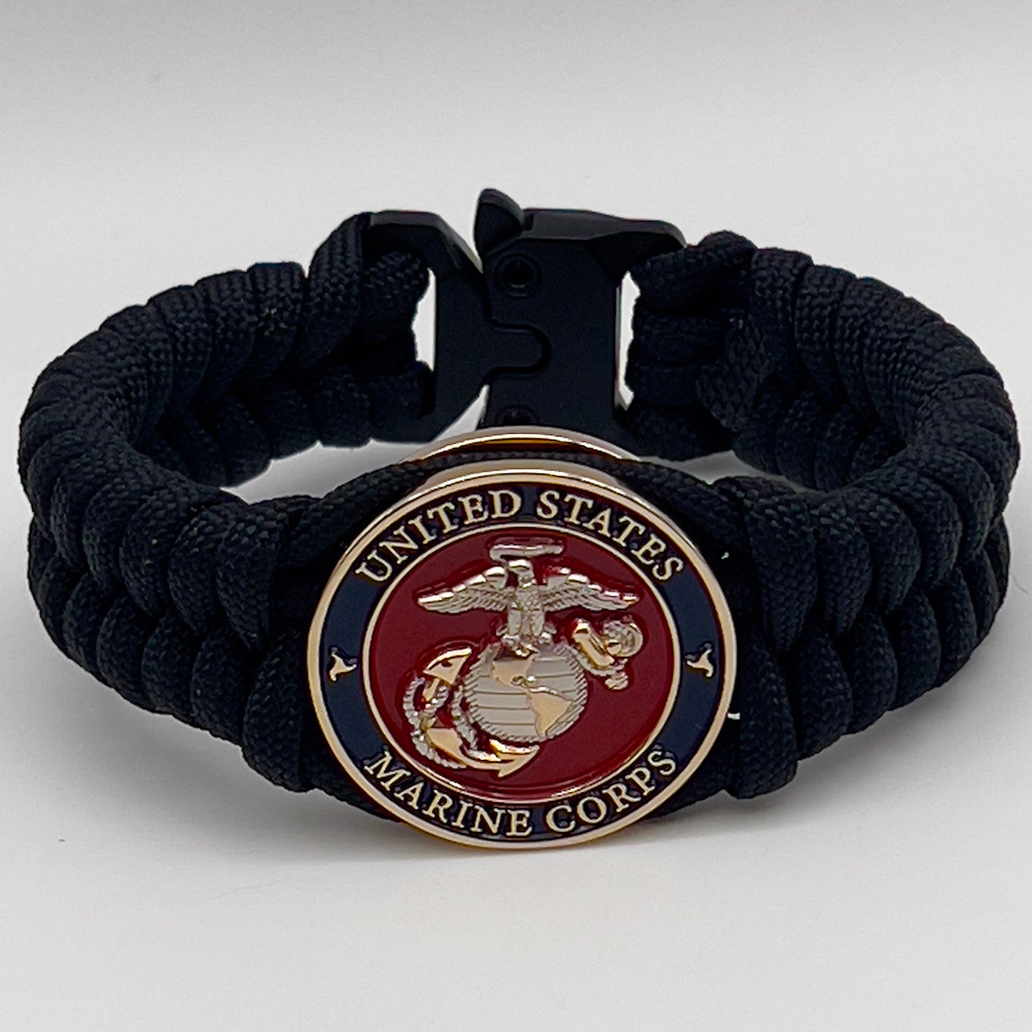 Thick, semi-rigid and comfortable braided United States Marine Corps bracelet featuring a 24K gold and silver plated USMC officer Eagle Globe and Anchor medallion, a black Cobra style tactical buckle and woven with black 550 paracord.