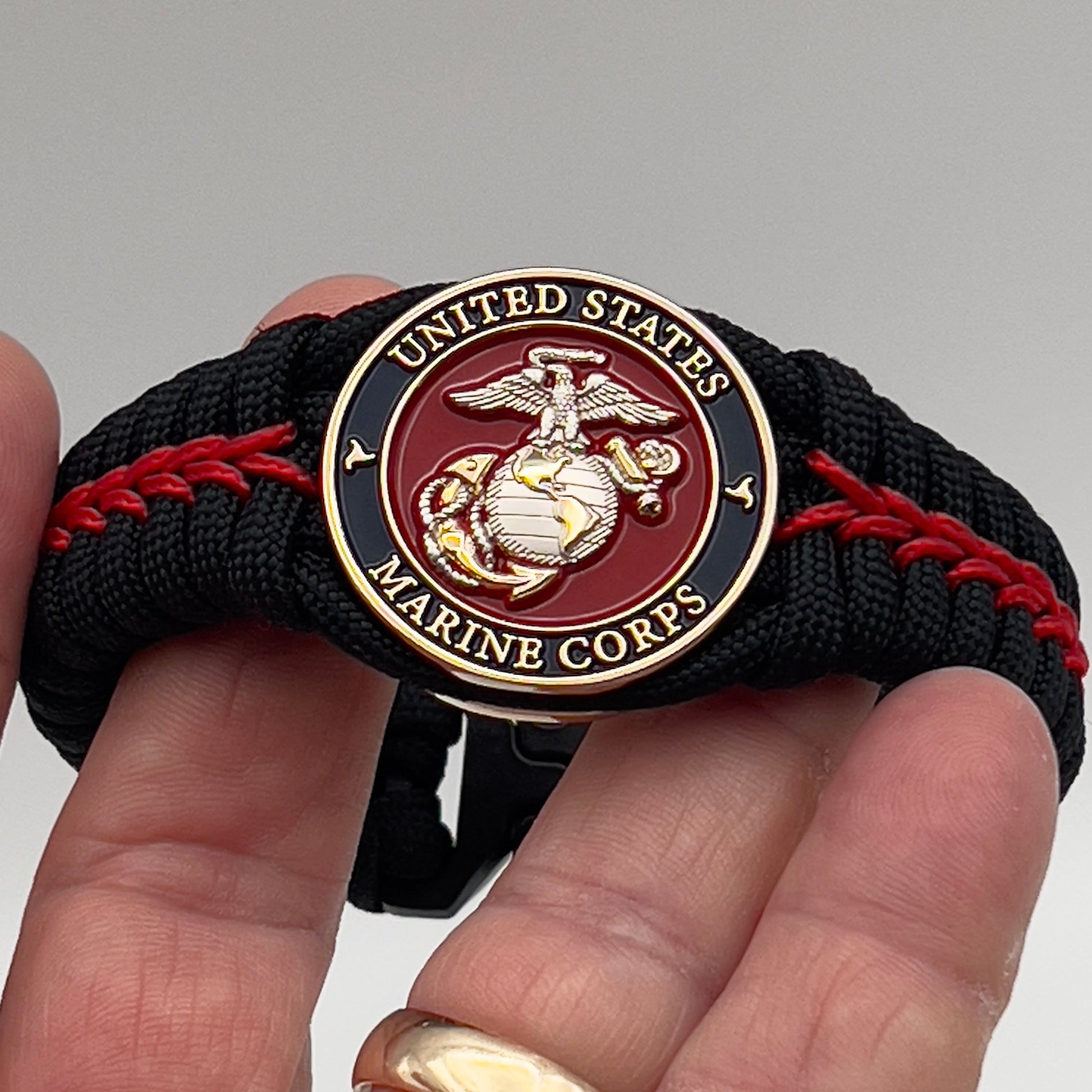 Thick, semi-rigid and comfortable braided United States Marine Corps bracelet featuring a 24K gold and silver plated USMC officer Eagle Globe and Anchor medallion, a black Cobra style tactical buckle and woven with black 550 and Imperial red micro paracord.
