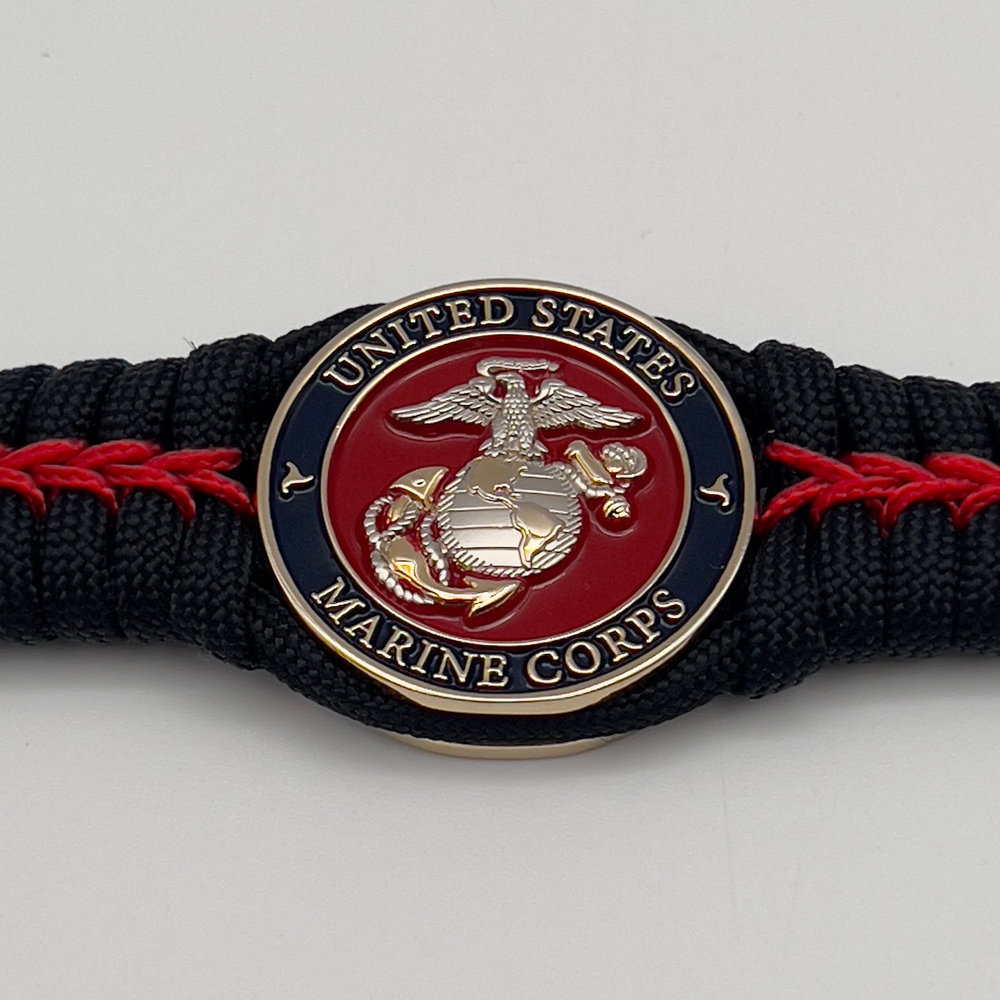 Thick, semi-rigid and comfortable braided United States Marine Corps bracelet featuring a 24K gold and silver plated USMC officer Eagle Globe and Anchor medallion, a black Cobra style tactical buckle and woven with black 550 and Imperial red micro paracord.