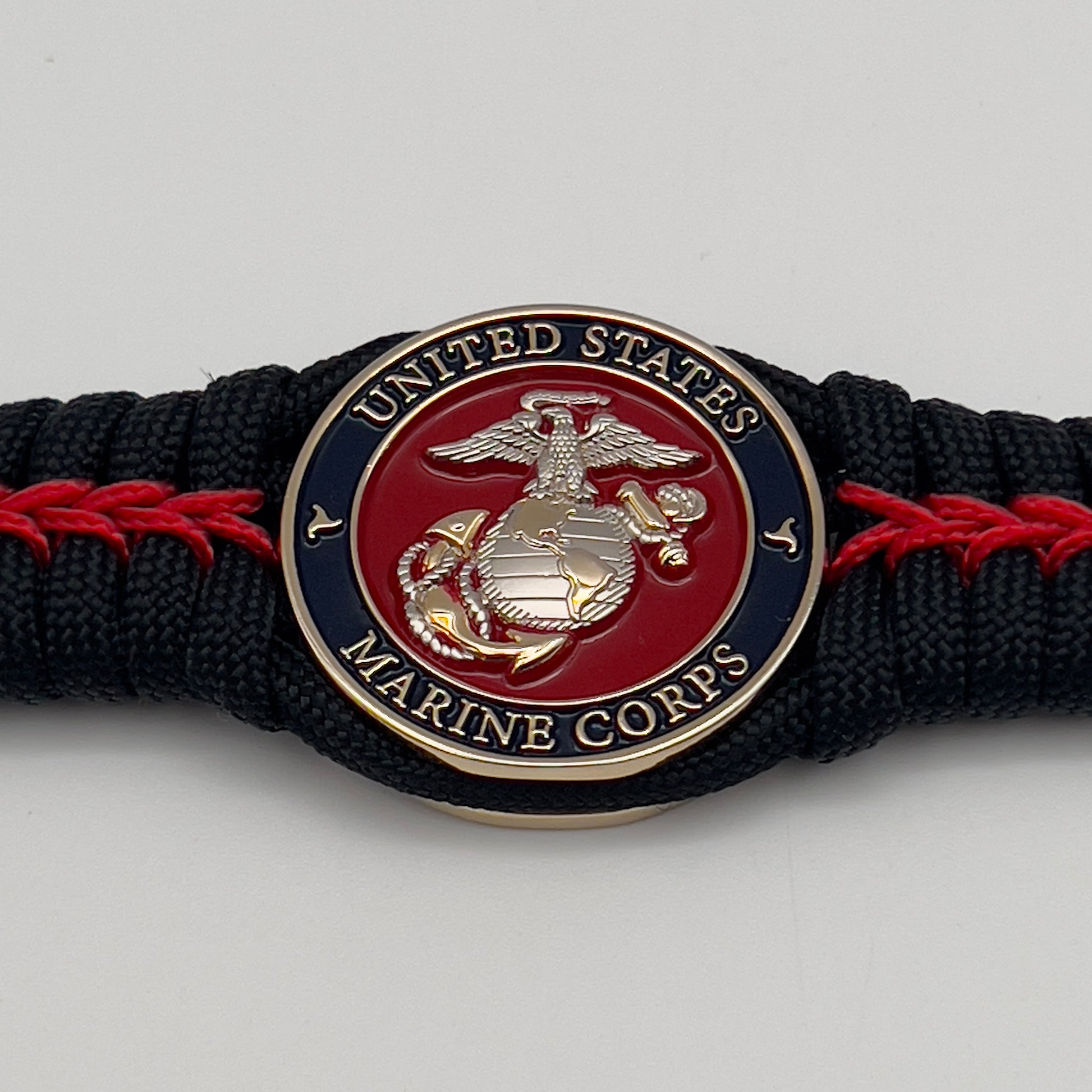 Thick, semi-rigid and comfortable braided United States Marine Corps bracelet featuring a 24K gold and silver plated USMC officer Eagle Globe and Anchor medallion, a black Cobra style tactical buckle and woven with black 550 and Imperial red micro paracord.
