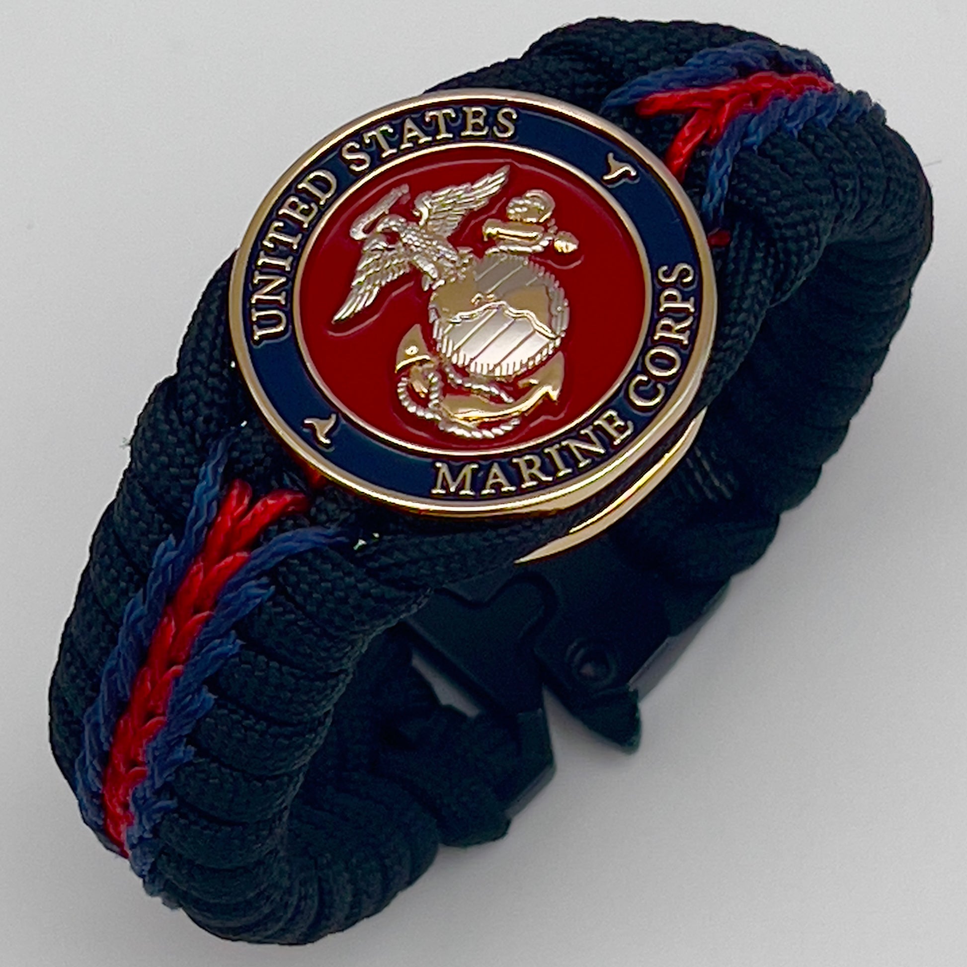Thick, semi-rigid and comfortable braided United States Marine Corps bracelet featuring a 24K gold and silver plated USMC officer Eagle Globe and Anchor medallion, a black Cobra style tactical buckle and woven with Navy blue, Imperial red and black paracord.