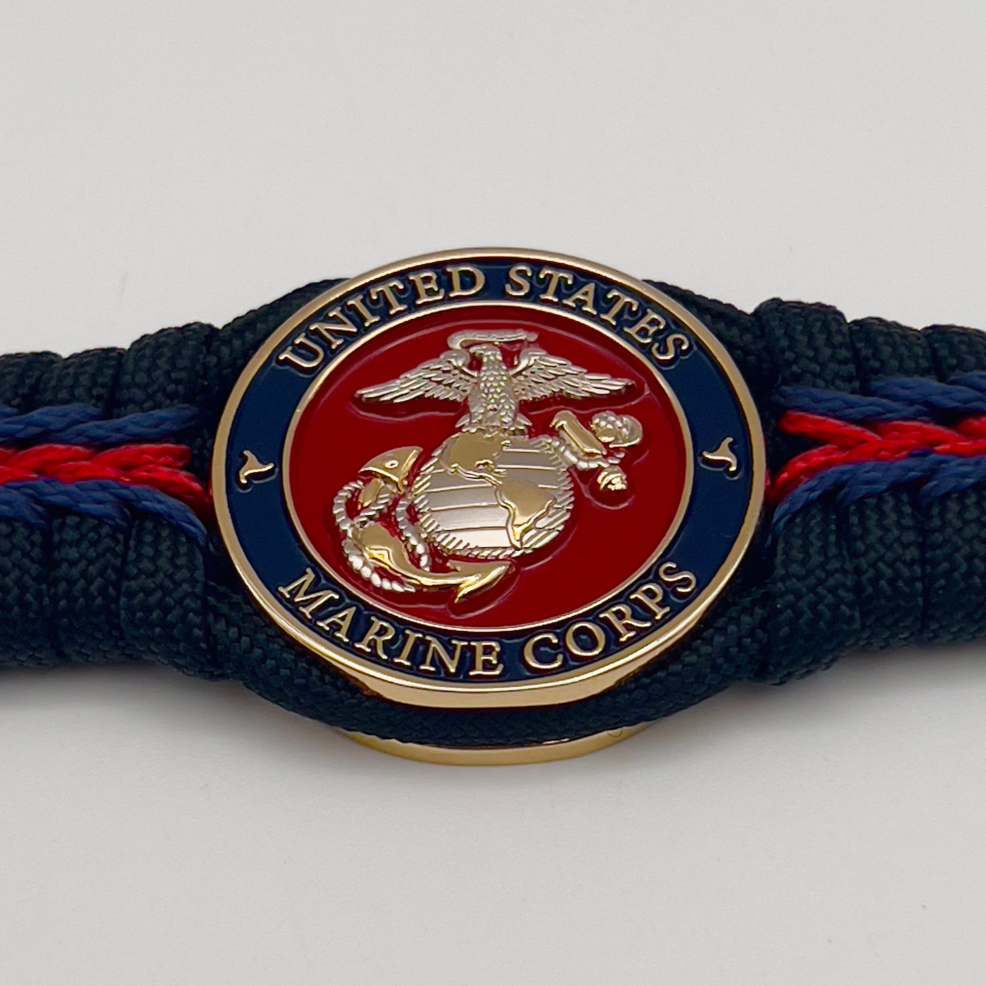 Thick, semi-rigid and comfortable braided United States Marine Corps bracelet featuring a 24K gold and silver plated USMC officer Eagle Globe and Anchor medallion, a black Cobra style tactical buckle and woven with Navy blue, Imperial red and black paracord.