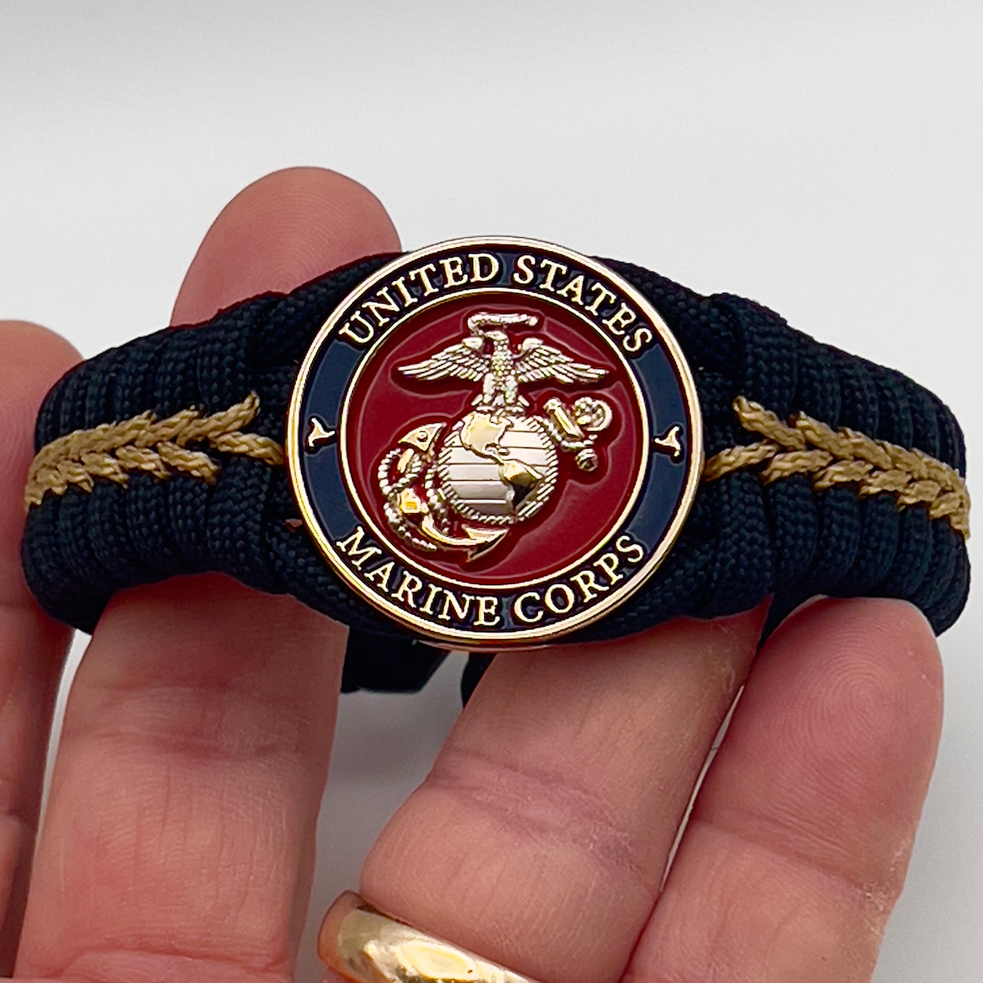 Thick, semi-rigid and comfortable braided United States Marine Corps bracelet featuring a 24K gold and silver plated USMC officer Eagle Globe and Anchor medallion, a black Cobra style tactical buckle and woven with black 550 and gold micro paracord.