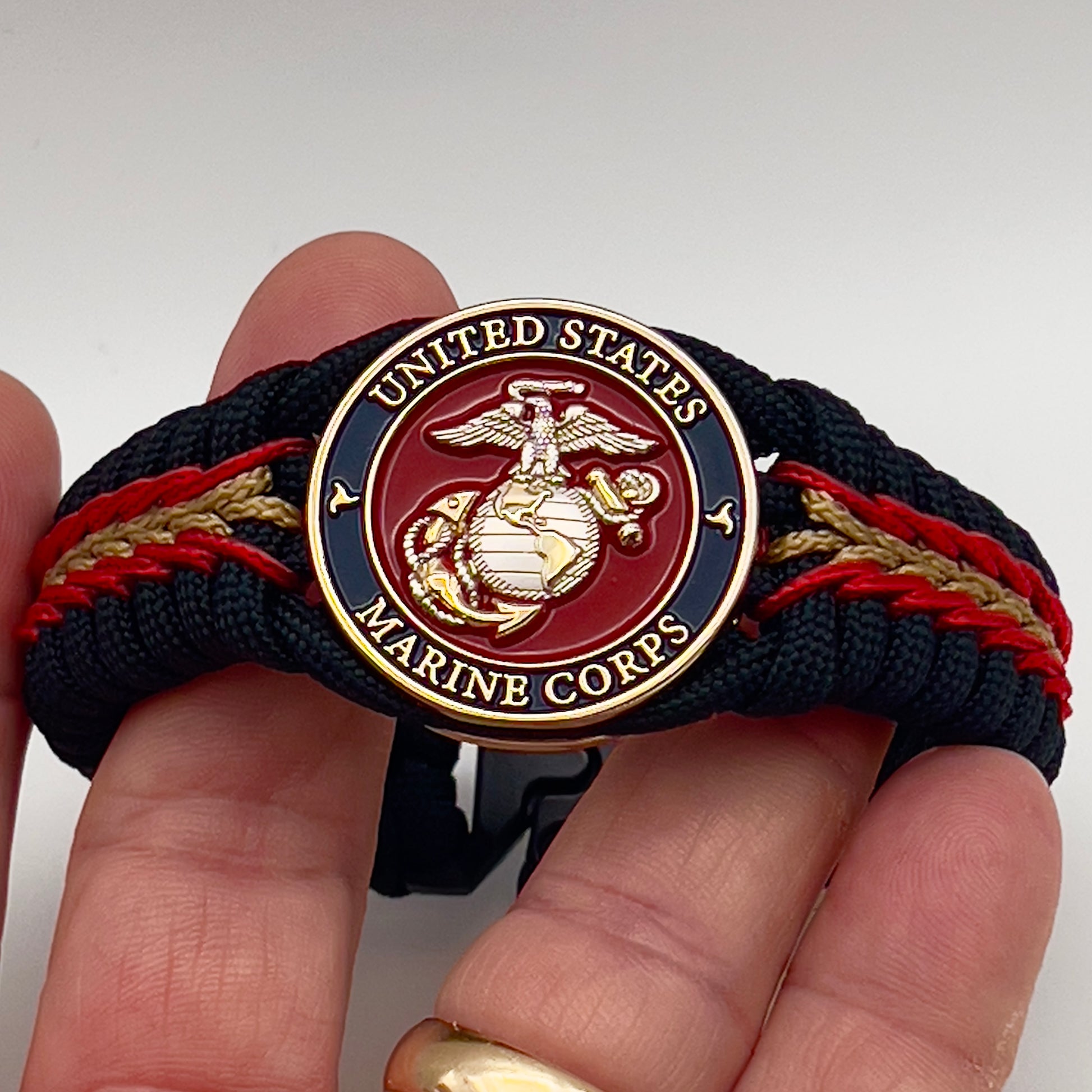 Thick, semi-rigid and comfortable braided United States Marine Corps bracelet featuring a 24K gold and silver plated USMC officer Eagle Globe and Anchor medallion, a black Cobra style tactical buckle and woven with black 550, Imperial red and gold micro paracord.