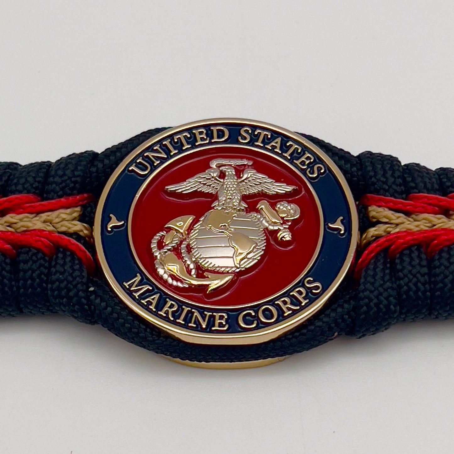 Thick, semi-rigid and comfortable braided United States Marine Corps bracelet featuring a 24K gold and silver plated USMC officer Eagle Globe and Anchor medallion, a black Cobra style tactical buckle and woven with black 550, Imperial red and gold micro paracord.