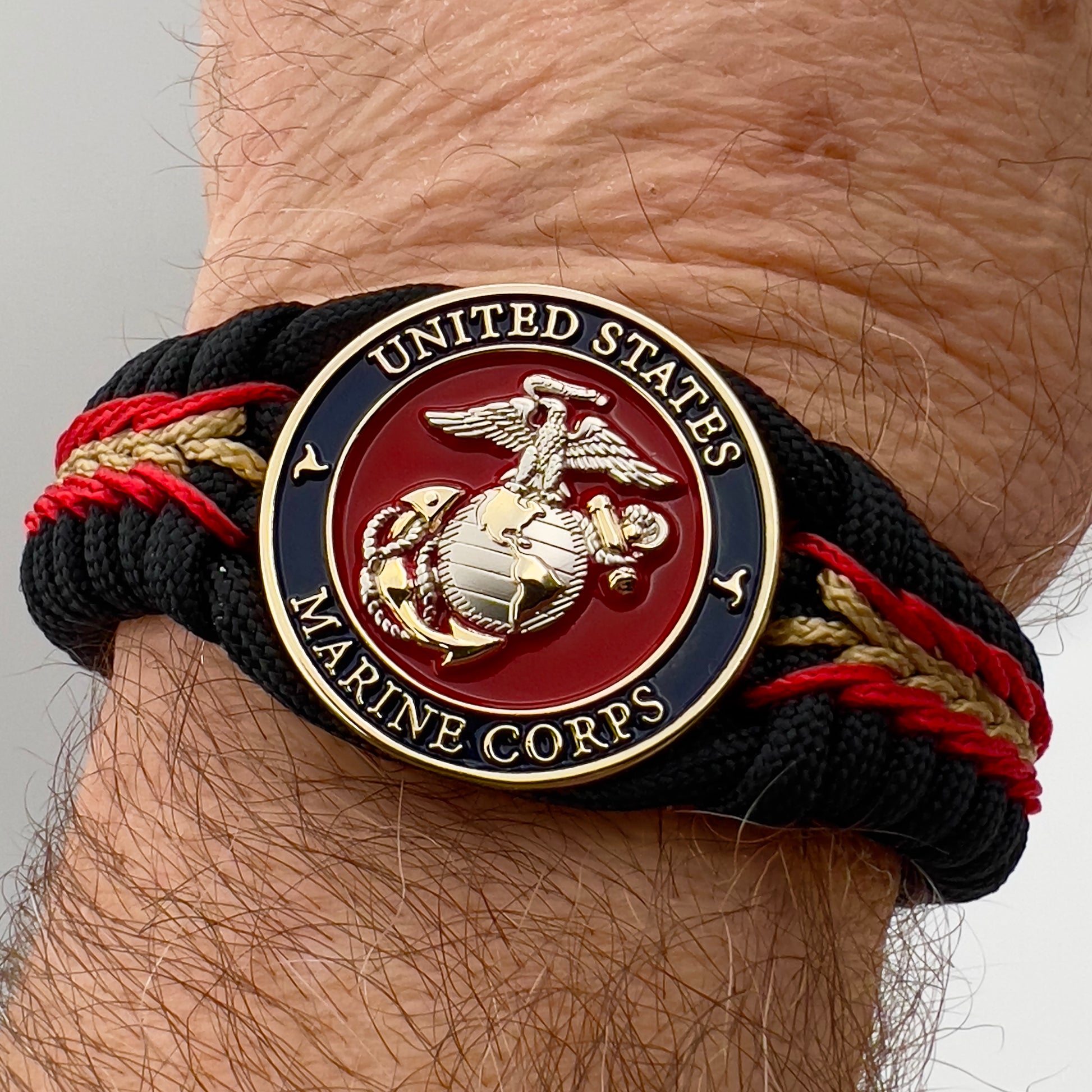 Thick, semi-rigid and comfortable braided United States Marine Corps bracelet featuring a 24K gold and silver plated USMC officer Eagle Globe and Anchor medallion, a black Cobra style tactical buckle and woven with black 550, Imperial red and gold micro paracord.