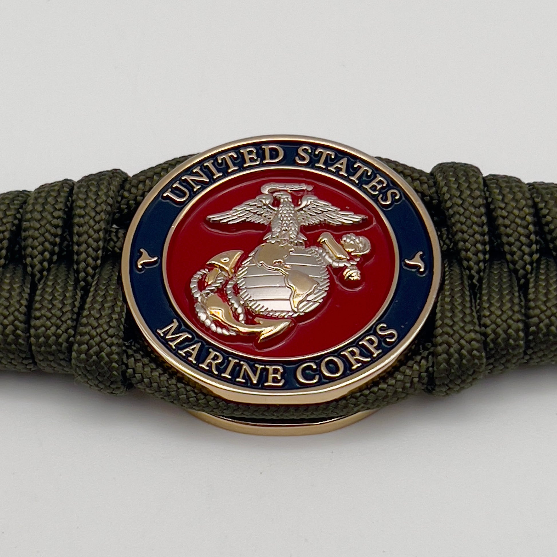 Thick, semi-rigid and comfortable braided United States Marine Corps bracelet featuring a 24K gold and silver plated USMC officer Eagle Globe and Anchor medallion, a gold Cobra style tactical buckle and woven with olive drab 550 paracord.