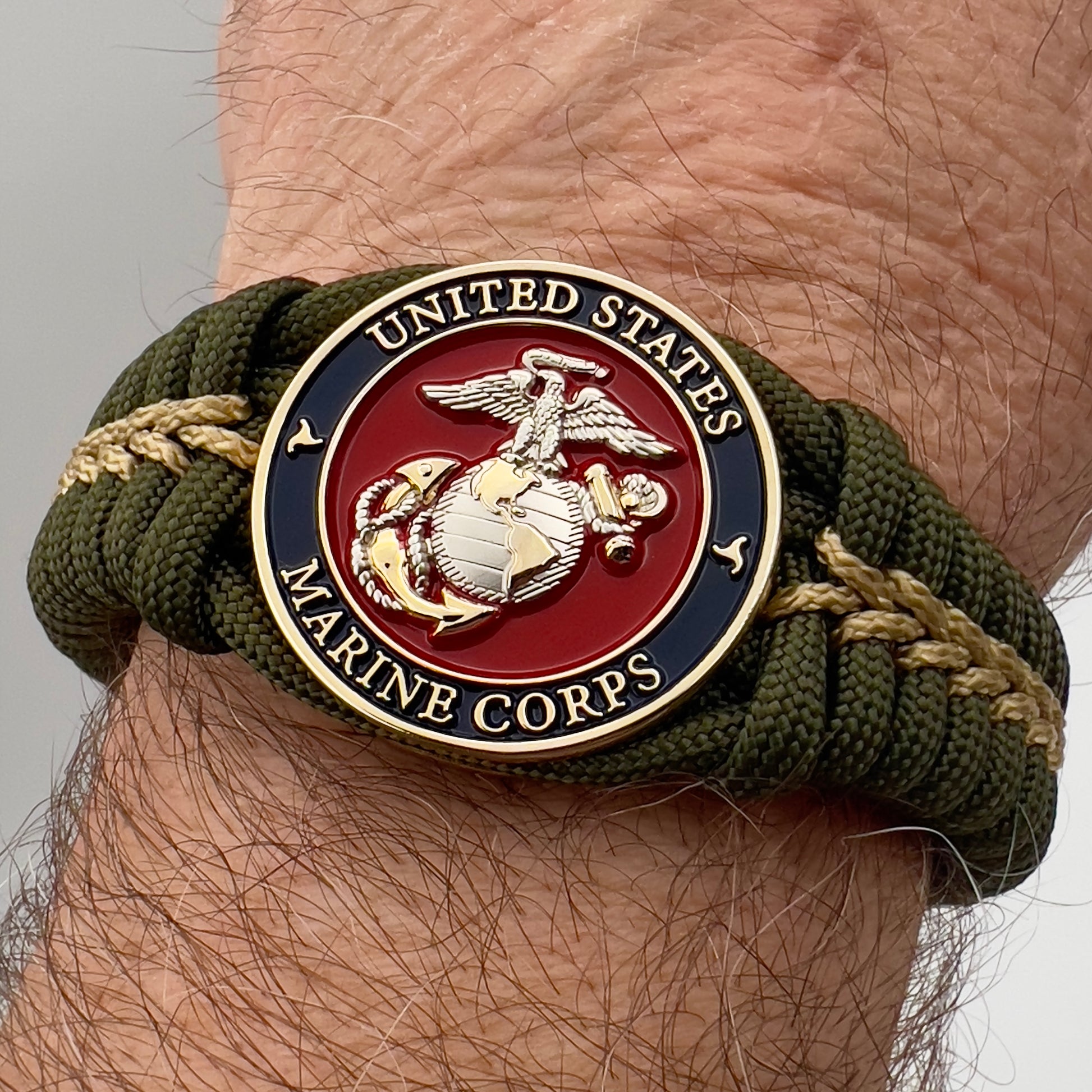 Thick, semi-rigid and comfortable braided United States Marine Corps bracelet featuring a 24K gold and silver plated USMC officer Eagle Globe and Anchor medallion, a gold Cobra style tactical buckle and woven with olive drab 550 and gold micro paracord.