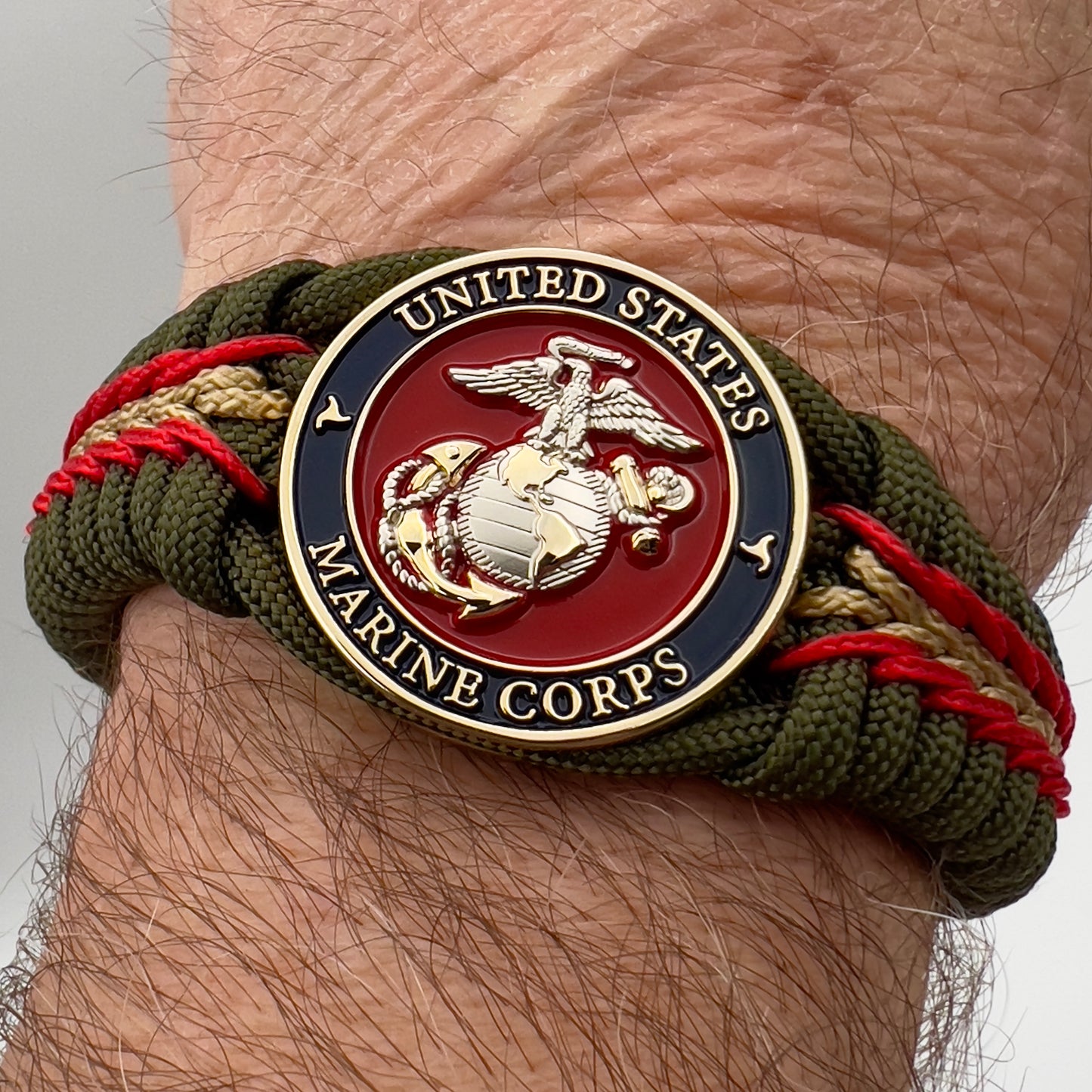 Thick, semi-rigid and comfortable braided United States Marine Corps bracelet featuring a 24K gold and silver plated USMC officer Eagle Globe and Anchor medallion, a gold Cobra style tactical buckle and woven with olive drab 550 and gold micro paracord.