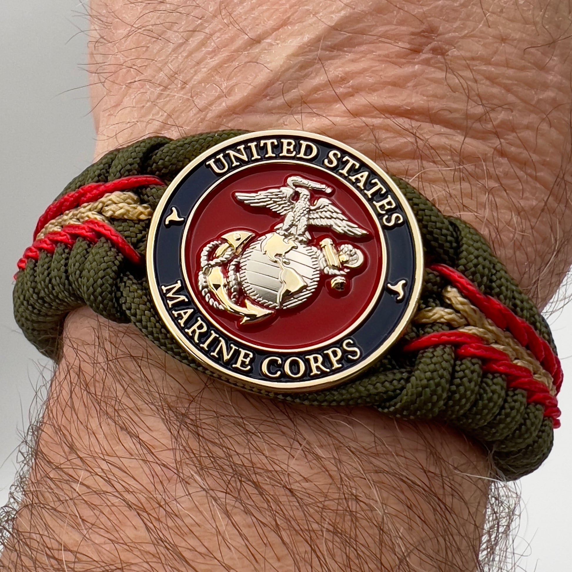 Thick, semi-rigid and comfortable braided United States Marine Corps bracelet featuring a 24K gold and silver plated USMC officer Eagle Globe and Anchor medallion, a gold Cobra style tactical buckle and woven with olive drab 550 and gold micro paracord.