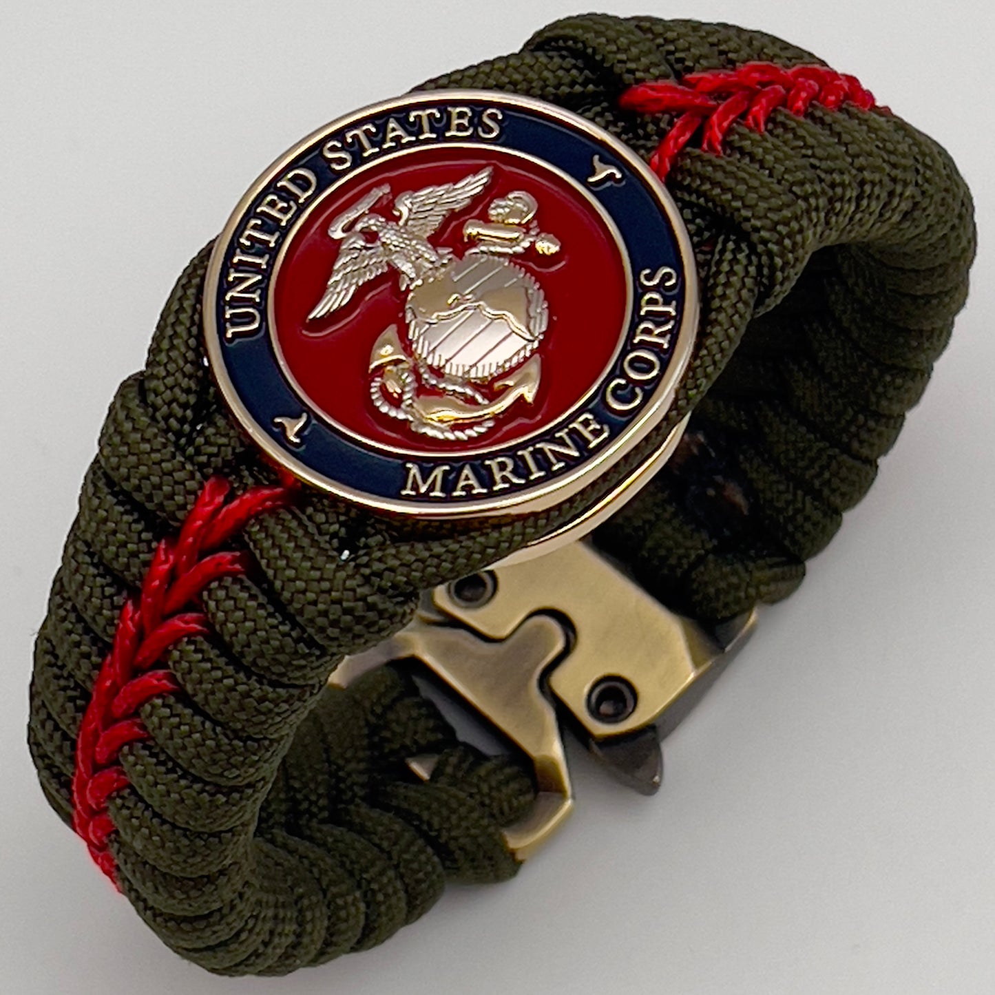 Thick, semi-rigid and comfortable braided United States Marine Corps bracelet featuring a 24K gold and silver plated USMC officer Eagle Globe and Anchor medallion, a gold Cobra style tactical buckle and woven with olive drab 550 and Imperial red micro paracord.
