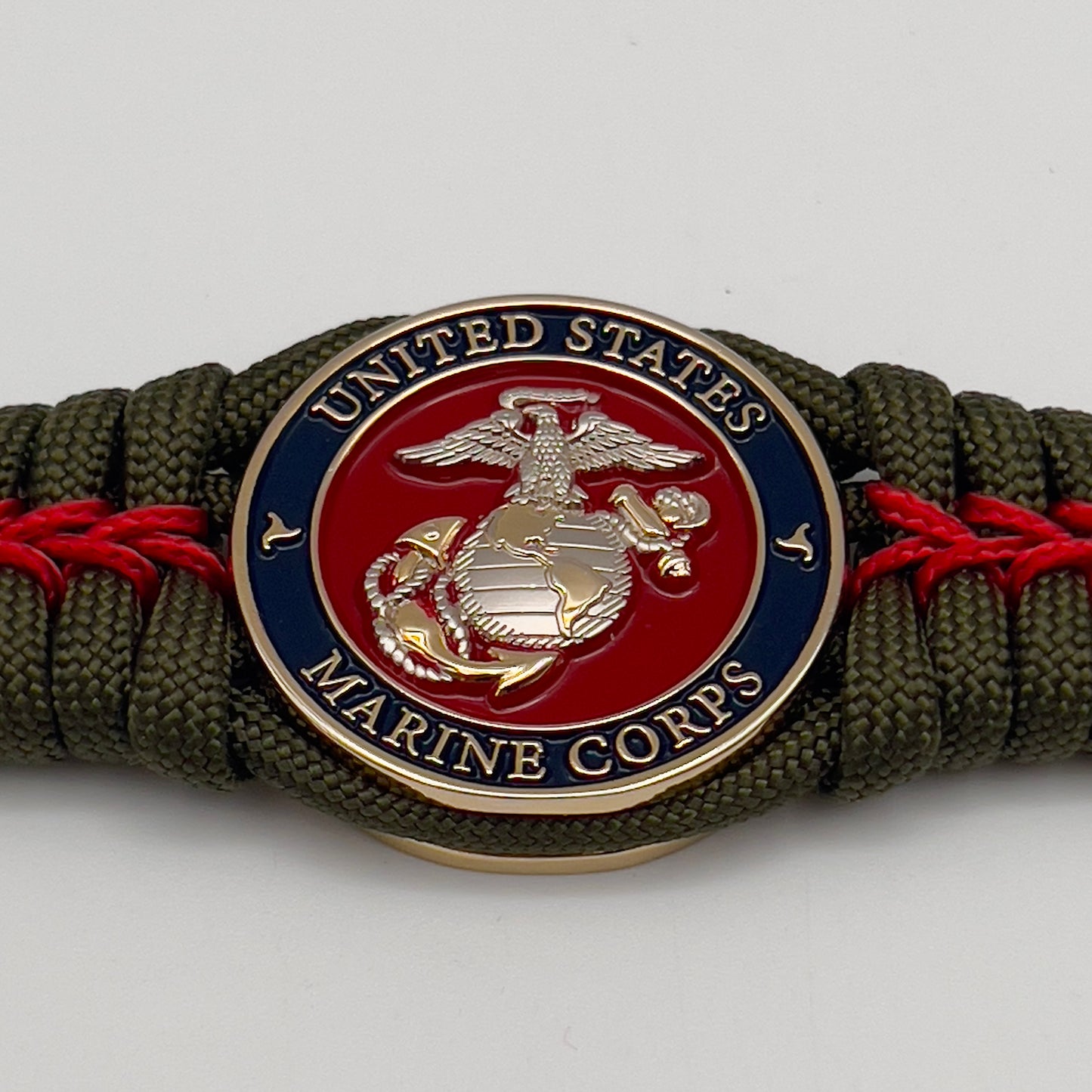Thick, semi-rigid and comfortable braided United States Marine Corps bracelet featuring a 24K gold and silver plated USMC officer Eagle Globe and Anchor medallion, a gold Cobra style tactical buckle and woven with olive drab 550 and Imperial red micro paracord.