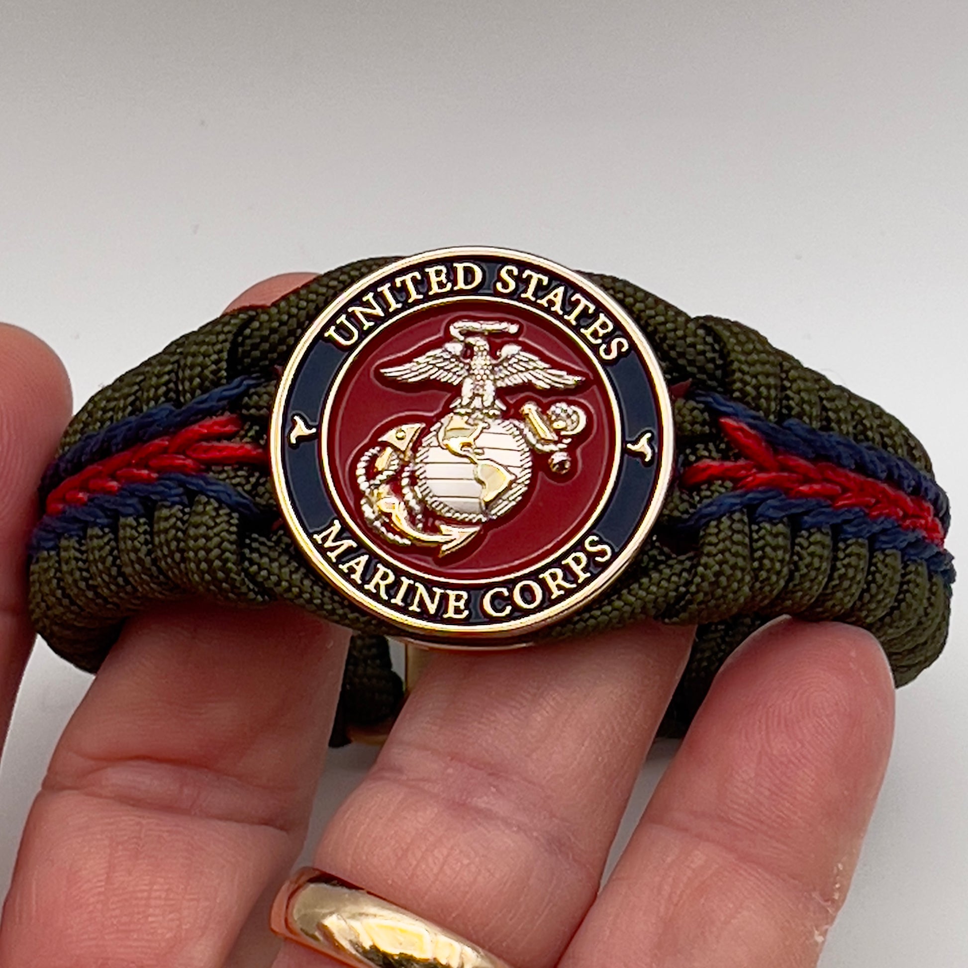 Thick, semi-rigid and comfortable braided United States Marine Corps bracelet featuring a 24K gold and silver plated USMC officer Eagle Globe and Anchor medallion, a gold Cobra style tactical buckle and woven with olive drab 550 and Imperial red and gold micro paracord.