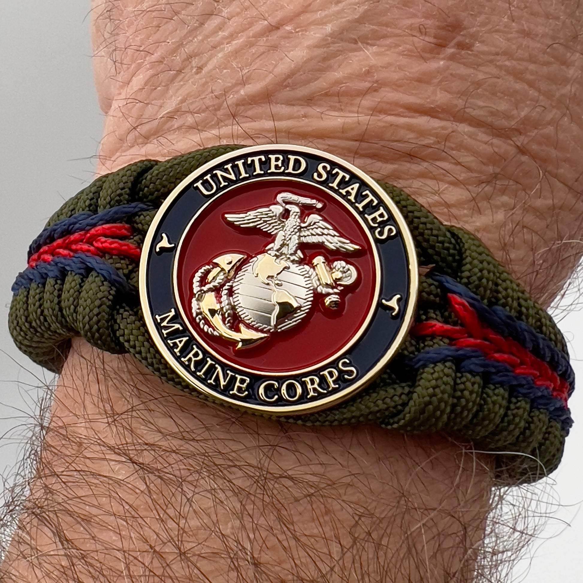 Thick, semi-rigid and comfortable braided United States Marine Corps bracelet featuring a 24K gold and silver plated USMC officer Eagle Globe and Anchor medallion, a gold Cobra style tactical buckle and woven with olive drab 550 and Imperial red and gold micro paracord.