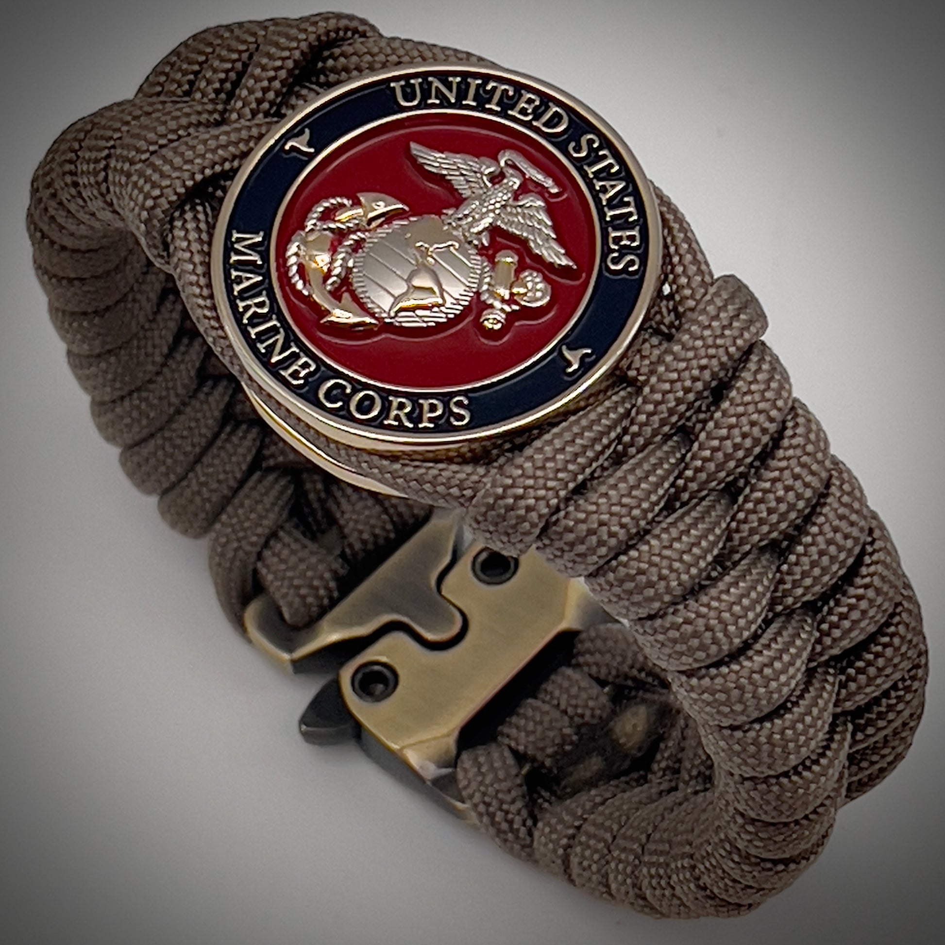Thick, semi-rigid and comfortable braided United States Marine Corps bracelet featuring a 24K gold and silver plated USMC officer Eagle Globe and Anchor medallion, a gold Cobra style tactical buckle and woven with tan 550 paracord.