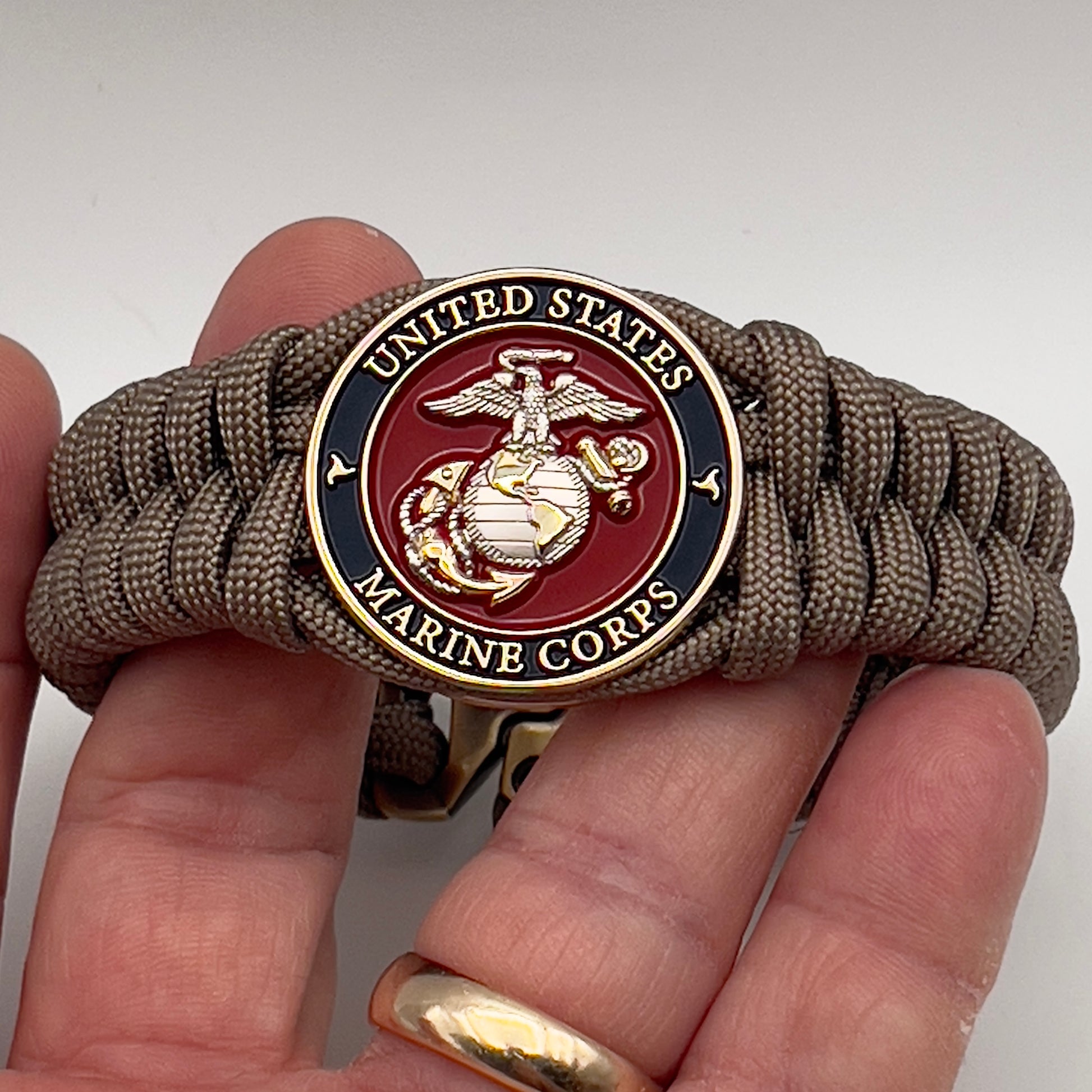 Thick, semi-rigid and comfortable braided United States Marine Corps bracelet featuring a 24K gold and silver plated USMC officer Eagle Globe and Anchor medallion, a gold Cobra style tactical buckle and woven with tan 550 paracord.