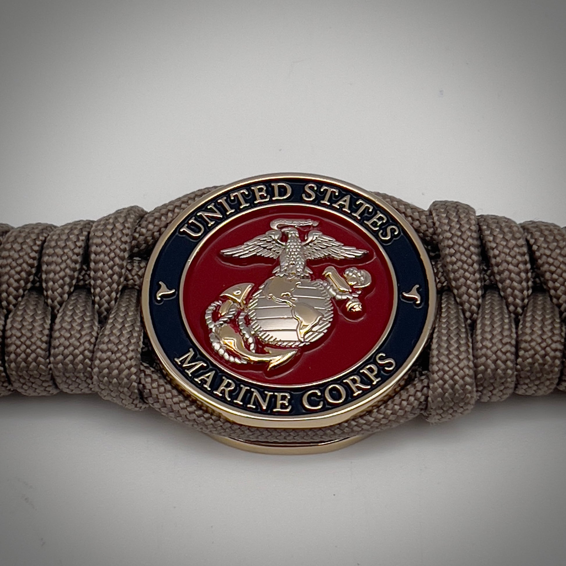 Thick, semi-rigid and comfortable braided United States Marine Corps bracelet featuring a 24K gold and silver plated USMC officer Eagle Globe and Anchor medallion, a gold Cobra style tactical buckle and woven with tan 550 paracord.