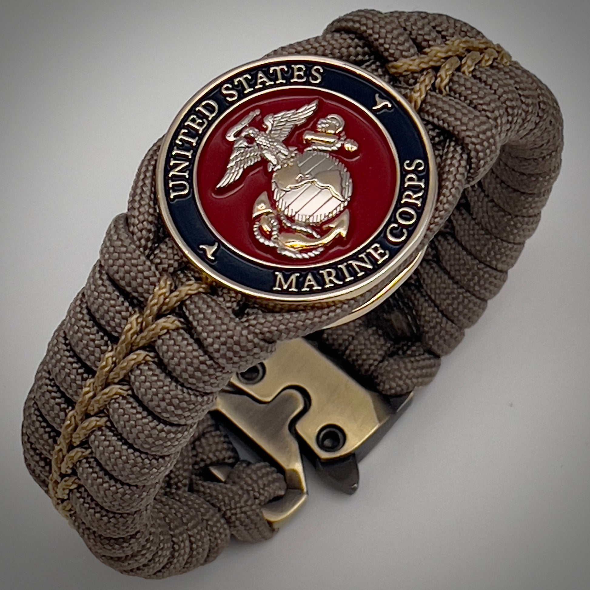 Thick, semi-rigid and comfortable braided United States Marine Corps bracelet featuring a 24K gold and silver plated USMC officer Eagle Globe and Anchor medallion, a gold Cobra style tactical buckle and woven with tan 550 paracord and gold micro cord.