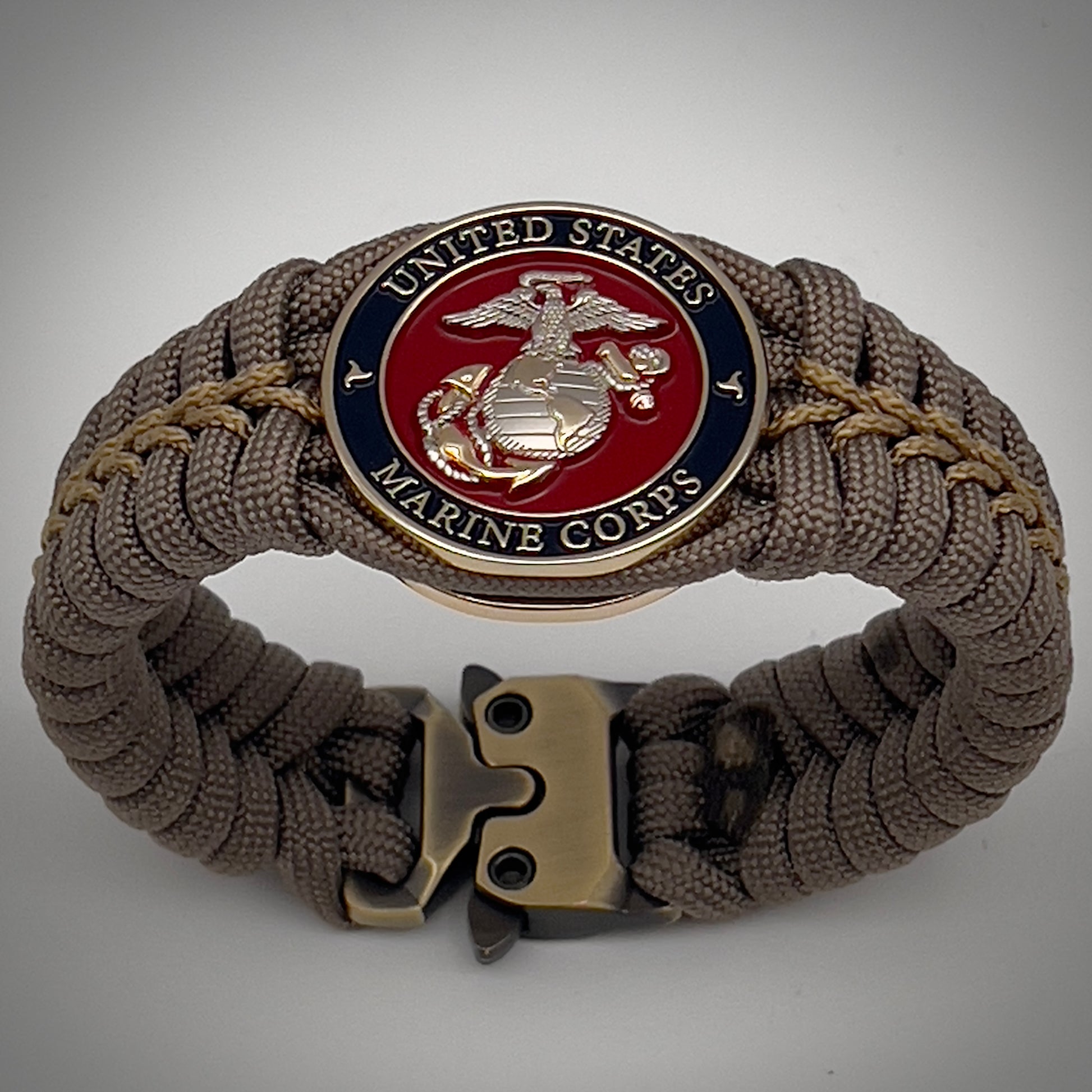 Thick, semi-rigid and comfortable braided United States Marine Corps bracelet featuring a 24K gold and silver plated USMC officer Eagle Globe and Anchor medallion, a gold Cobra style tactical buckle and woven with tan 550 paracord and gold micro cord.