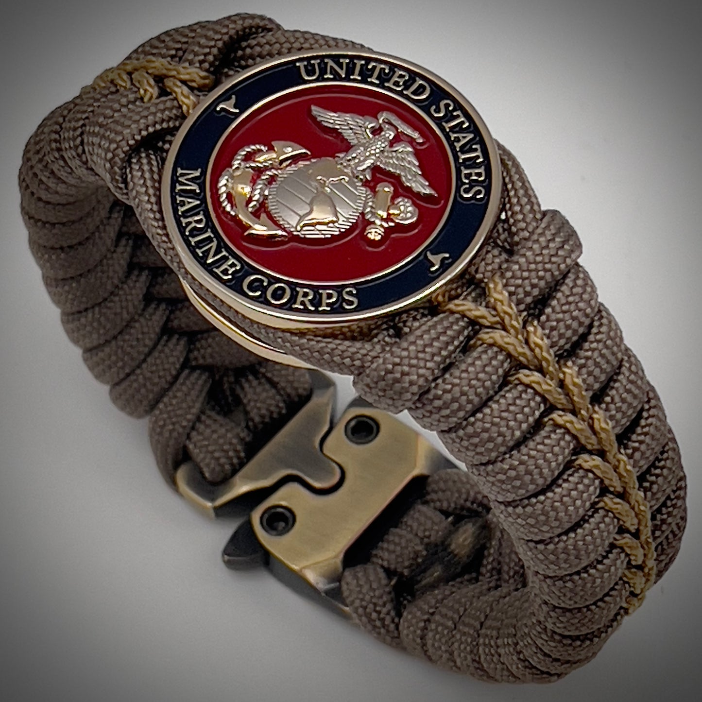 Thick, semi-rigid and comfortable braided United States Marine Corps bracelet featuring a 24K gold and silver plated USMC officer Eagle Globe and Anchor medallion, a gold Cobra style tactical buckle and woven with tan 550 paracord and gold micro cord.