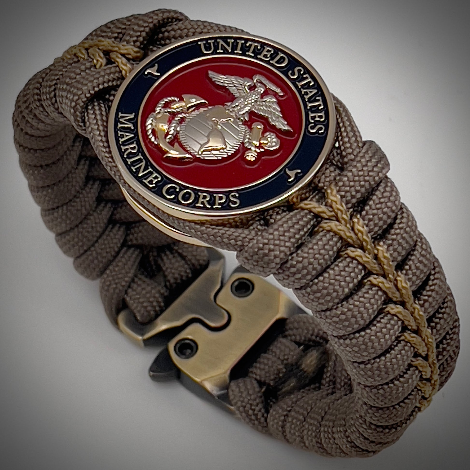 Thick, semi-rigid and comfortable braided United States Marine Corps bracelet featuring a 24K gold and silver plated USMC officer Eagle Globe and Anchor medallion, a gold Cobra style tactical buckle and woven with tan 550 paracord and gold micro cord.
