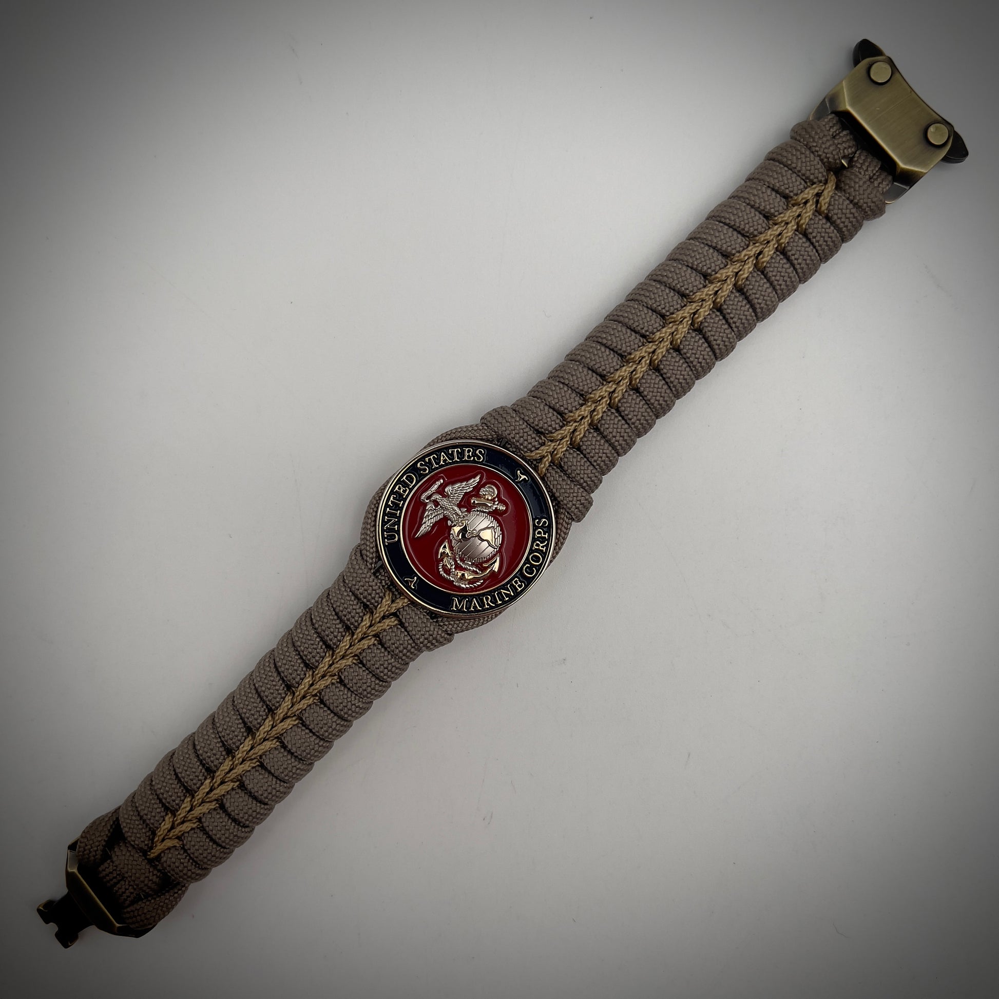 Thick, semi-rigid and comfortable braided United States Marine Corps bracelet featuring a 24K gold and silver plated USMC officer Eagle Globe and Anchor medallion, a gold Cobra style tactical buckle and woven with tan 550 paracord and gold micro cord.