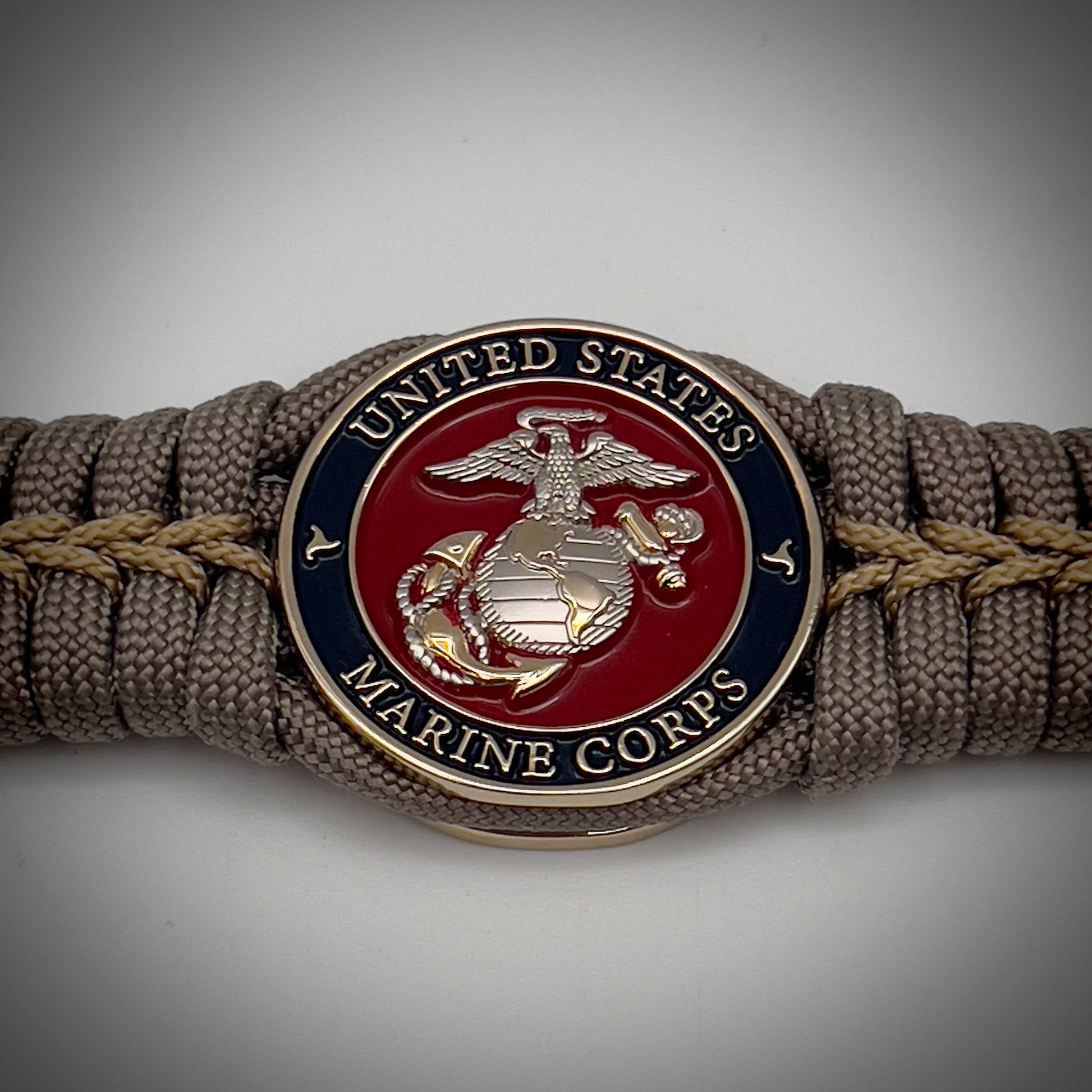 Thick, semi-rigid and comfortable braided United States Marine Corps bracelet featuring a 24K gold and silver plated USMC officer Eagle Globe and Anchor medallion, a gold Cobra style tactical buckle and woven with tan 550 paracord and gold micro cord.