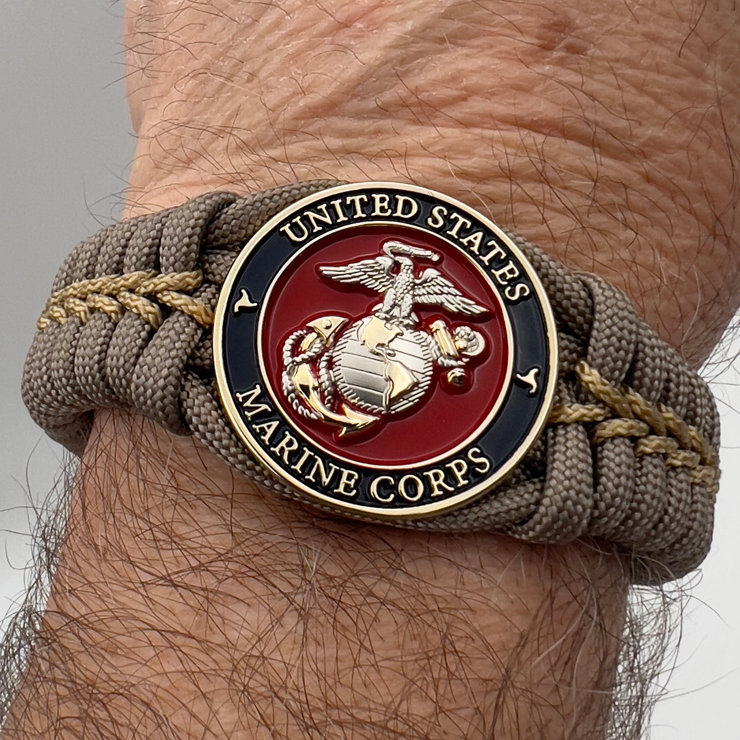 Thick, semi-rigid and comfortable braided United States Marine Corps bracelet featuring a 24K gold and silver plated USMC officer Eagle Globe and Anchor medallion, a gold Cobra style tactical buckle and woven with tan 550 paracord and gold micro cord.