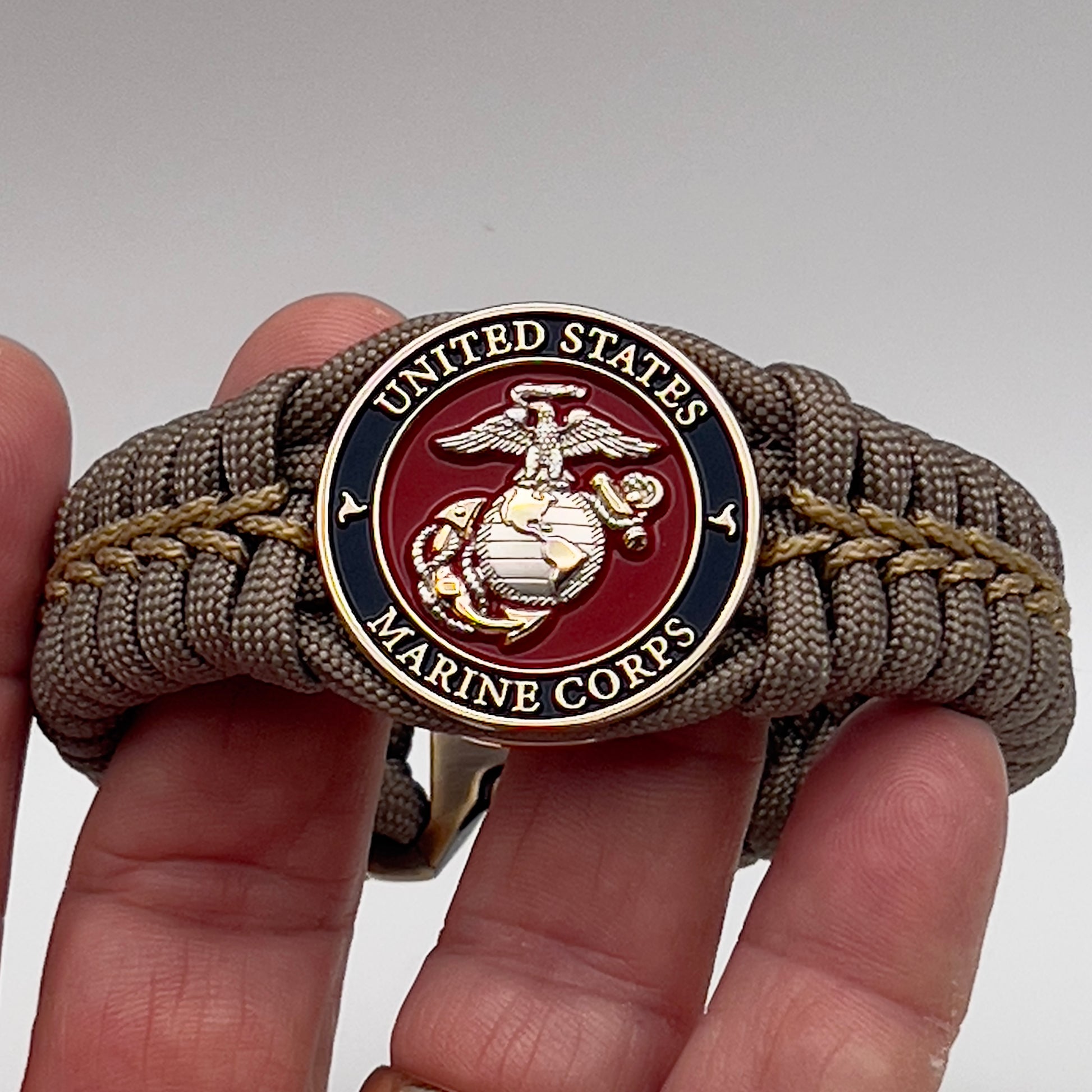 Thick, semi-rigid and comfortable braided United States Marine Corps bracelet featuring a 24K gold and silver plated USMC officer Eagle Globe and Anchor medallion, a gold Cobra style tactical buckle and woven with tan 550 paracord and gold micro cord.