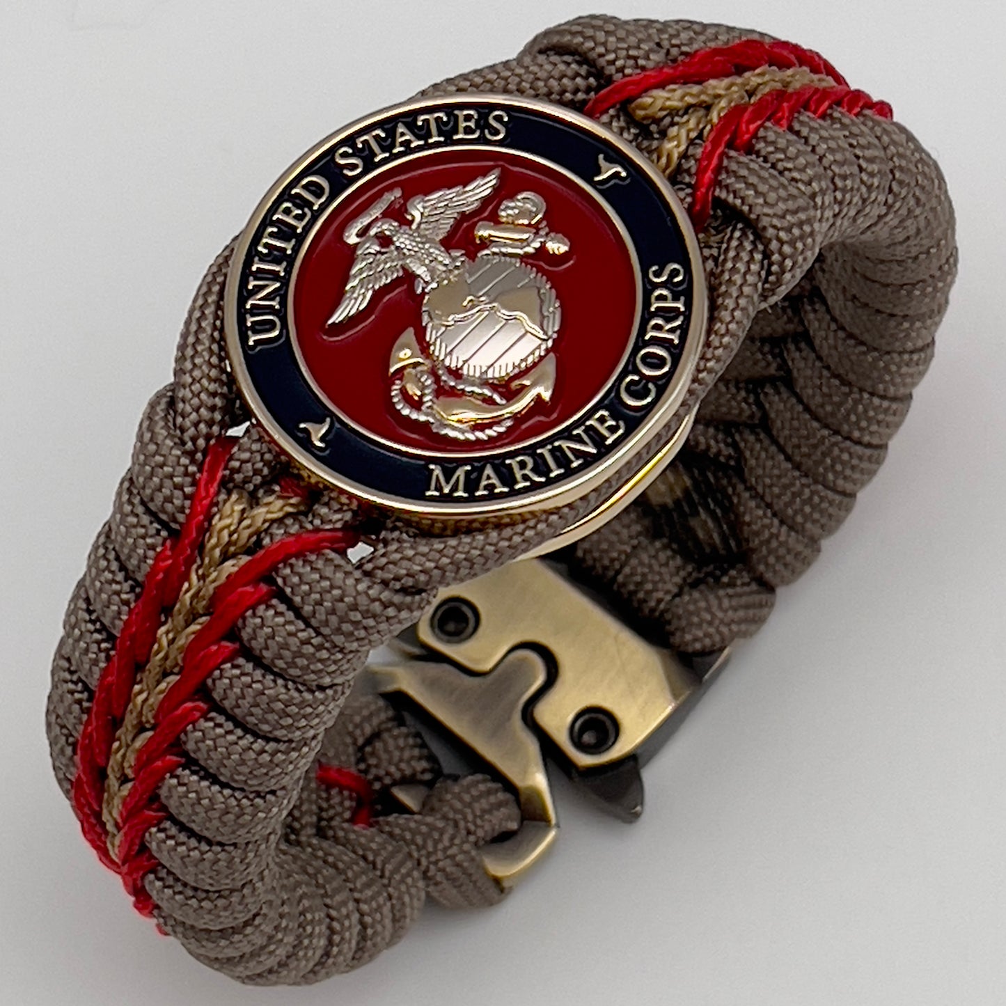 Thick and comfortable braided United States Marine Corps bracelet featuring a 24K gold and silver plated USMC officer Eagle Globe and Anchor medallion, a Cobra style tactical buckle and woven with tan 550, Imperial red and gold micro paracord.