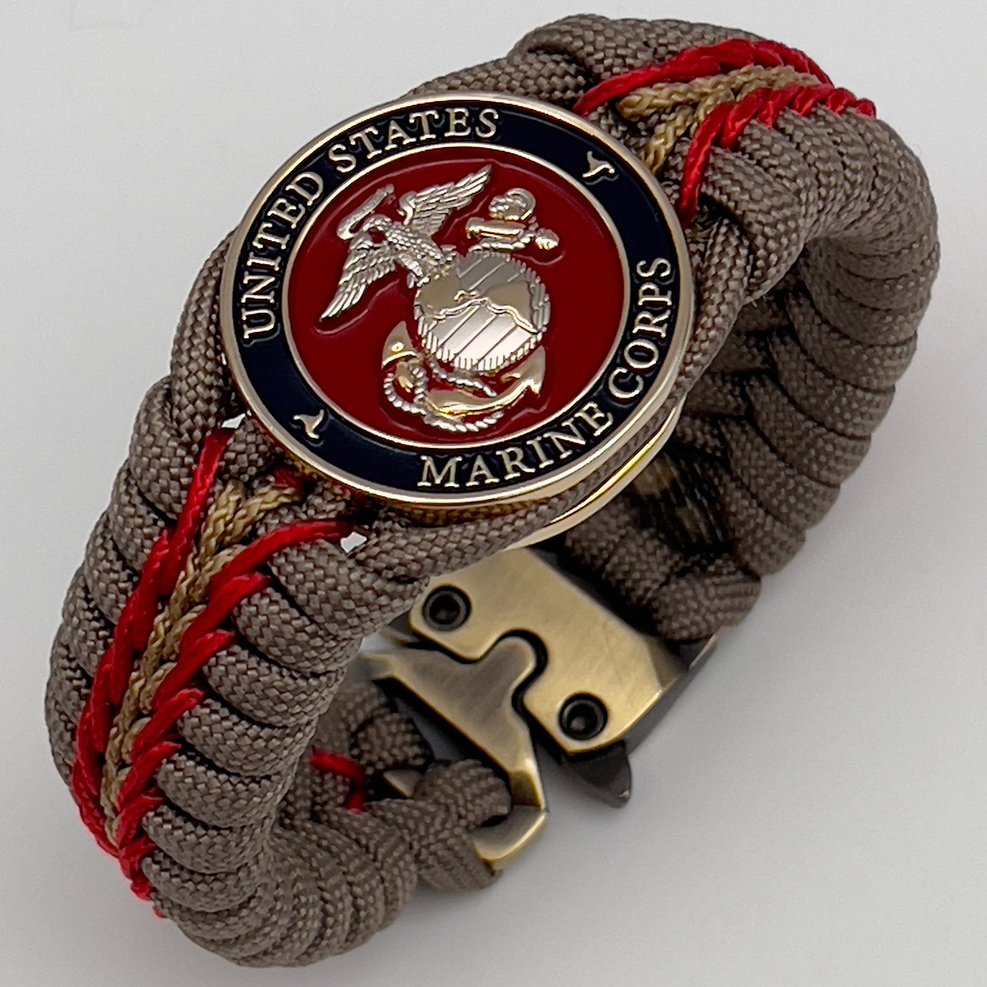 Thick and comfortable braided United States Marine Corps bracelet featuring a 24K gold and silver plated USMC officer Eagle Globe and Anchor medallion, a Cobra style tactical buckle and woven with tan 550, Imperial red and gold micro paracord.