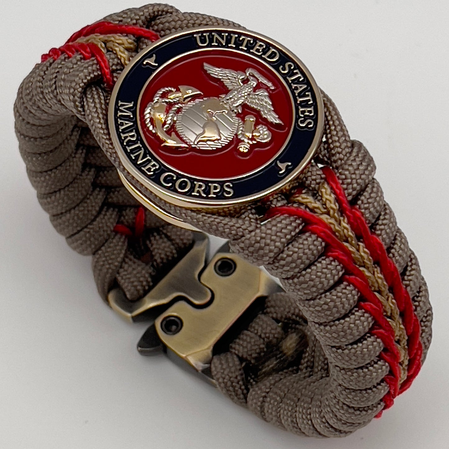 Thick and comfortable braided United States Marine Corps bracelet featuring a 24K gold and silver plated USMC officer Eagle Globe and Anchor medallion, a Cobra style tactical buckle and woven with tan 550, Imperial red and gold micro paracord.