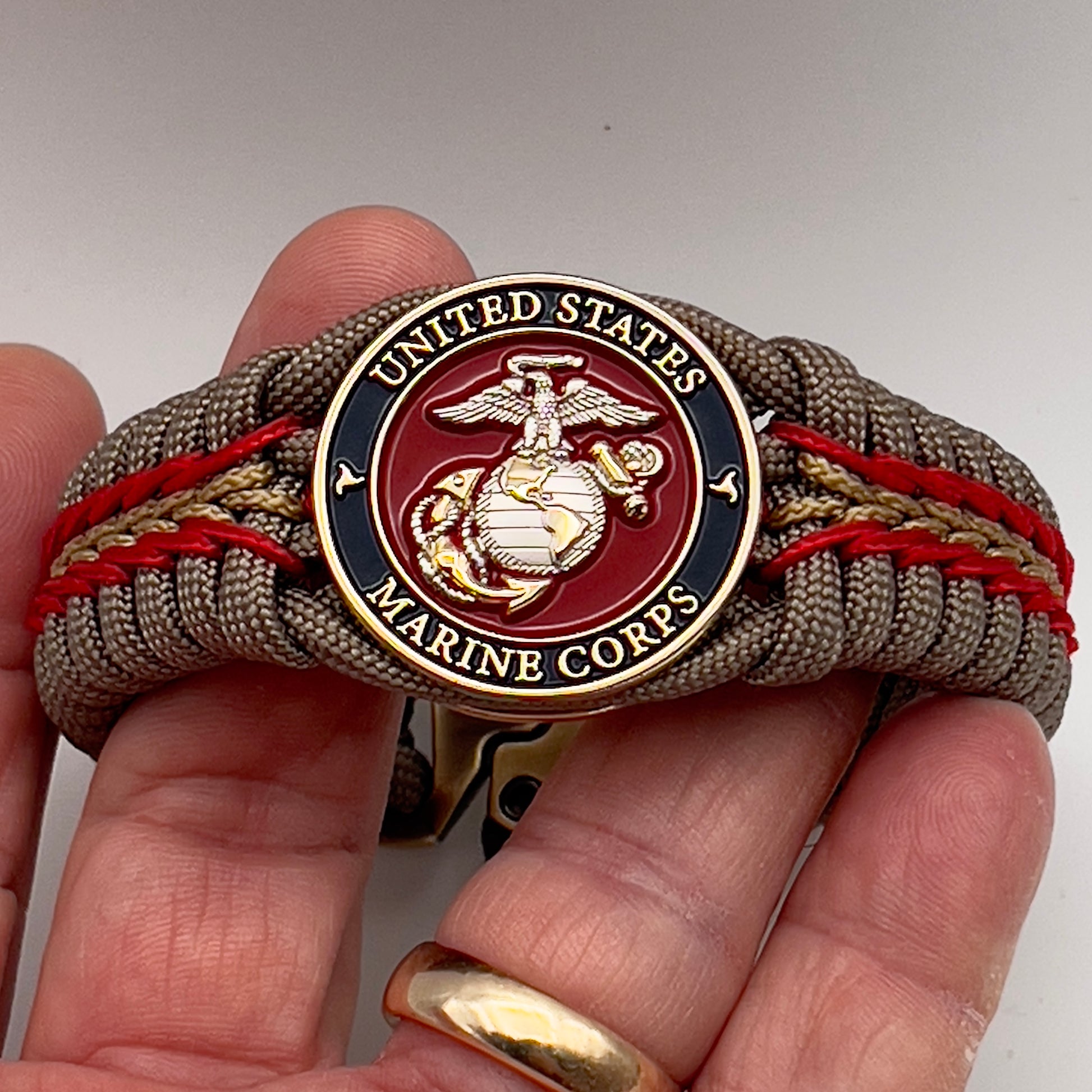 Thick and comfortable braided United States Marine Corps bracelet featuring a 24K gold and silver plated USMC officer Eagle Globe and Anchor medallion, a Cobra style tactical buckle and woven with tan 550, Imperial red and gold micro paracord.