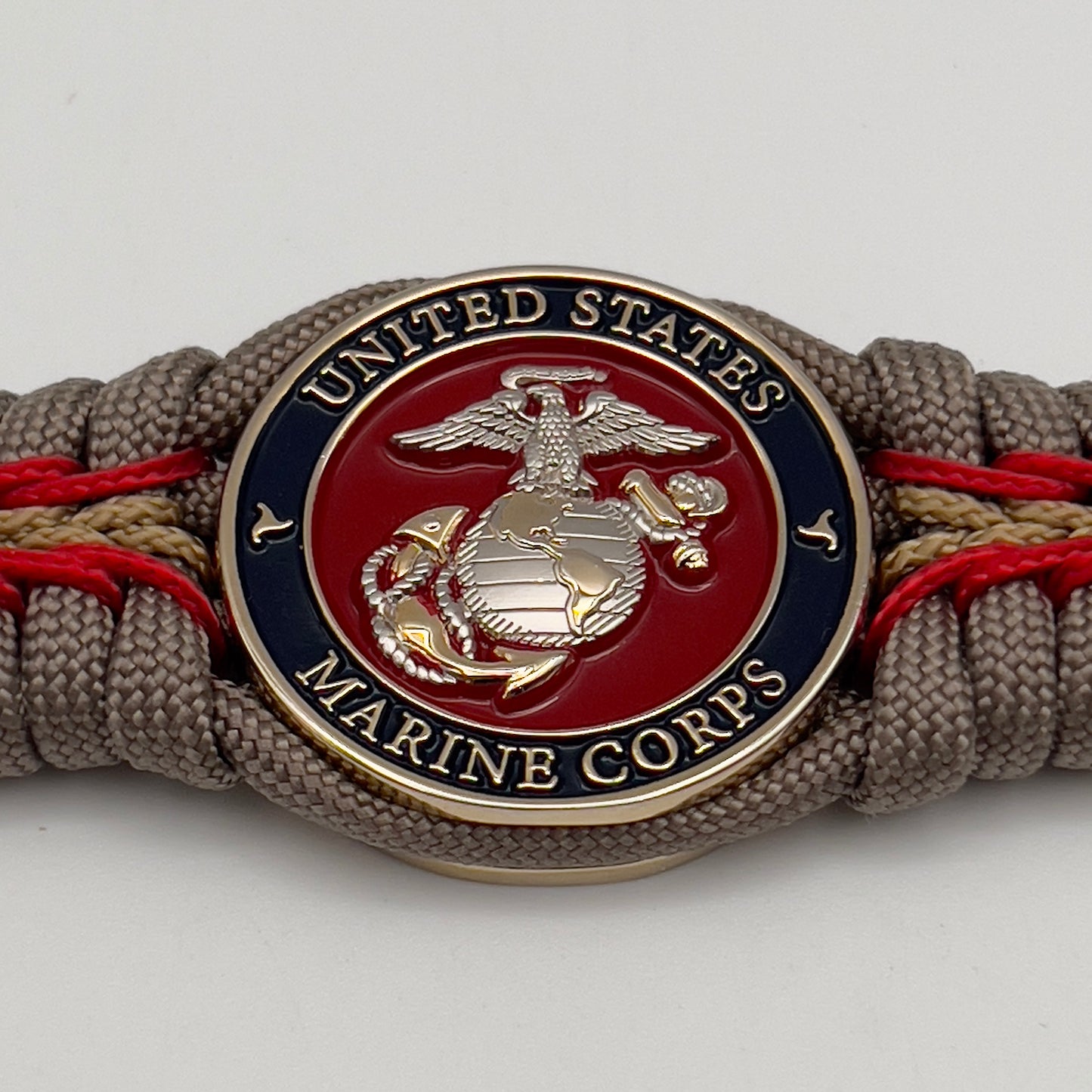 Thick and comfortable braided United States Marine Corps bracelet featuring a 24K gold and silver plated USMC officer Eagle Globe and Anchor medallion, a Cobra style tactical buckle and woven with tan 550, Imperial red and gold micro paracord.